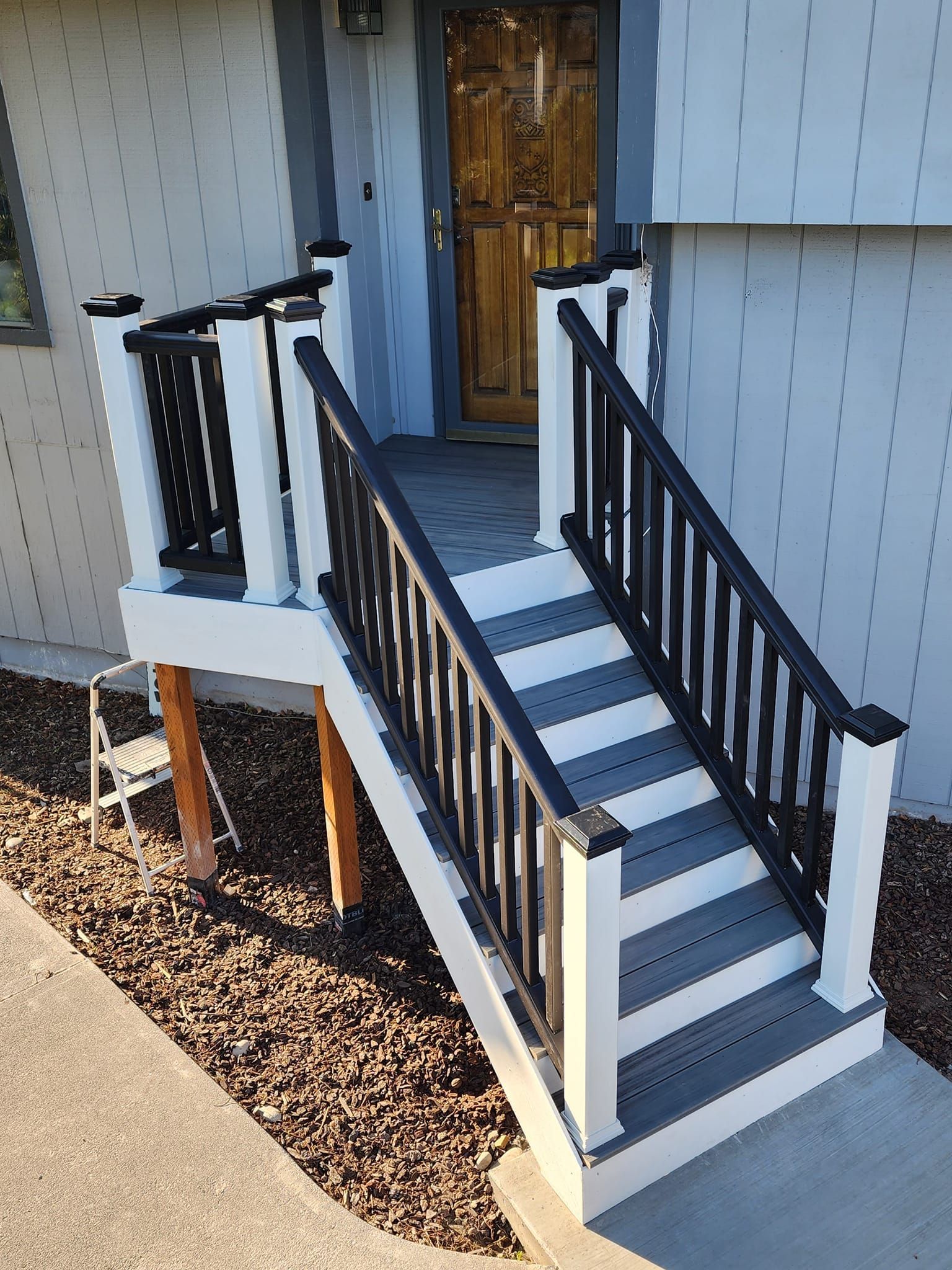 A raised deck with steps leading to a front door. White framing with black railings and gray steps.