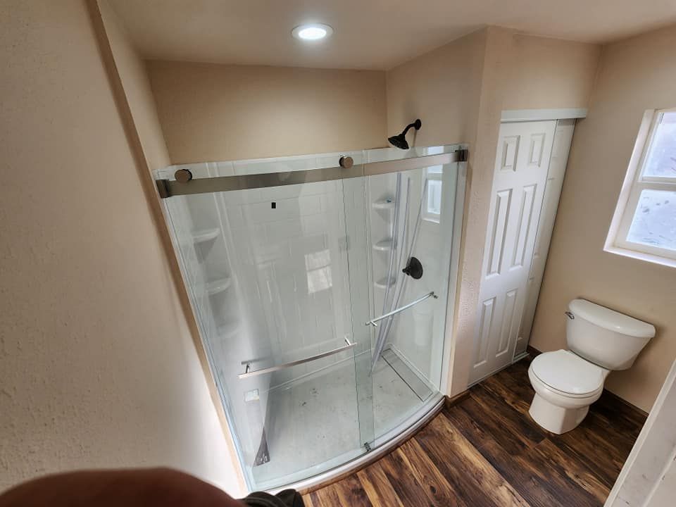 Bathroom with a glass shower, toilet, and wooden-look flooring. Beige walls.