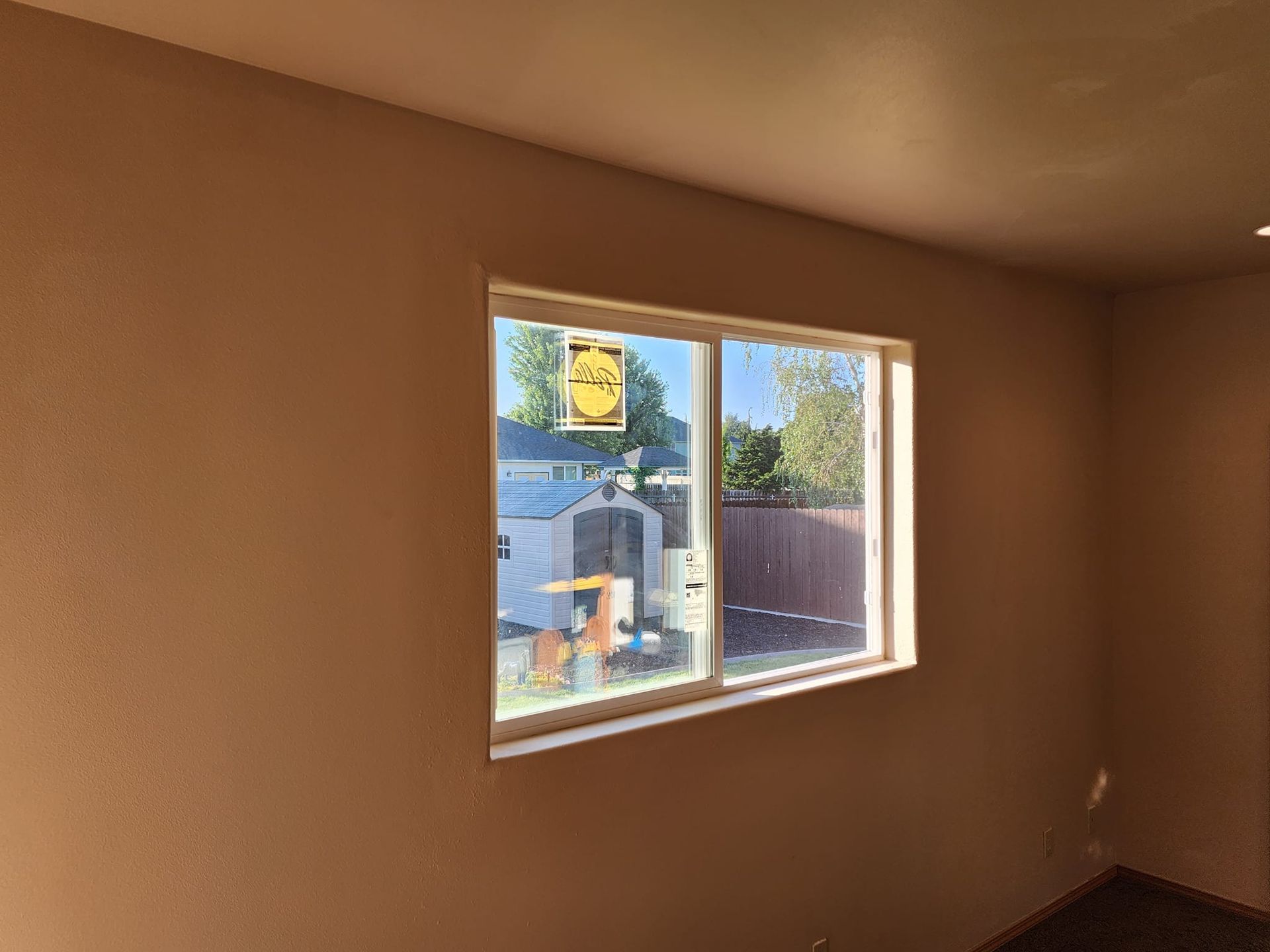 Room interior with a window; tan walls and trim, view of a backyard.