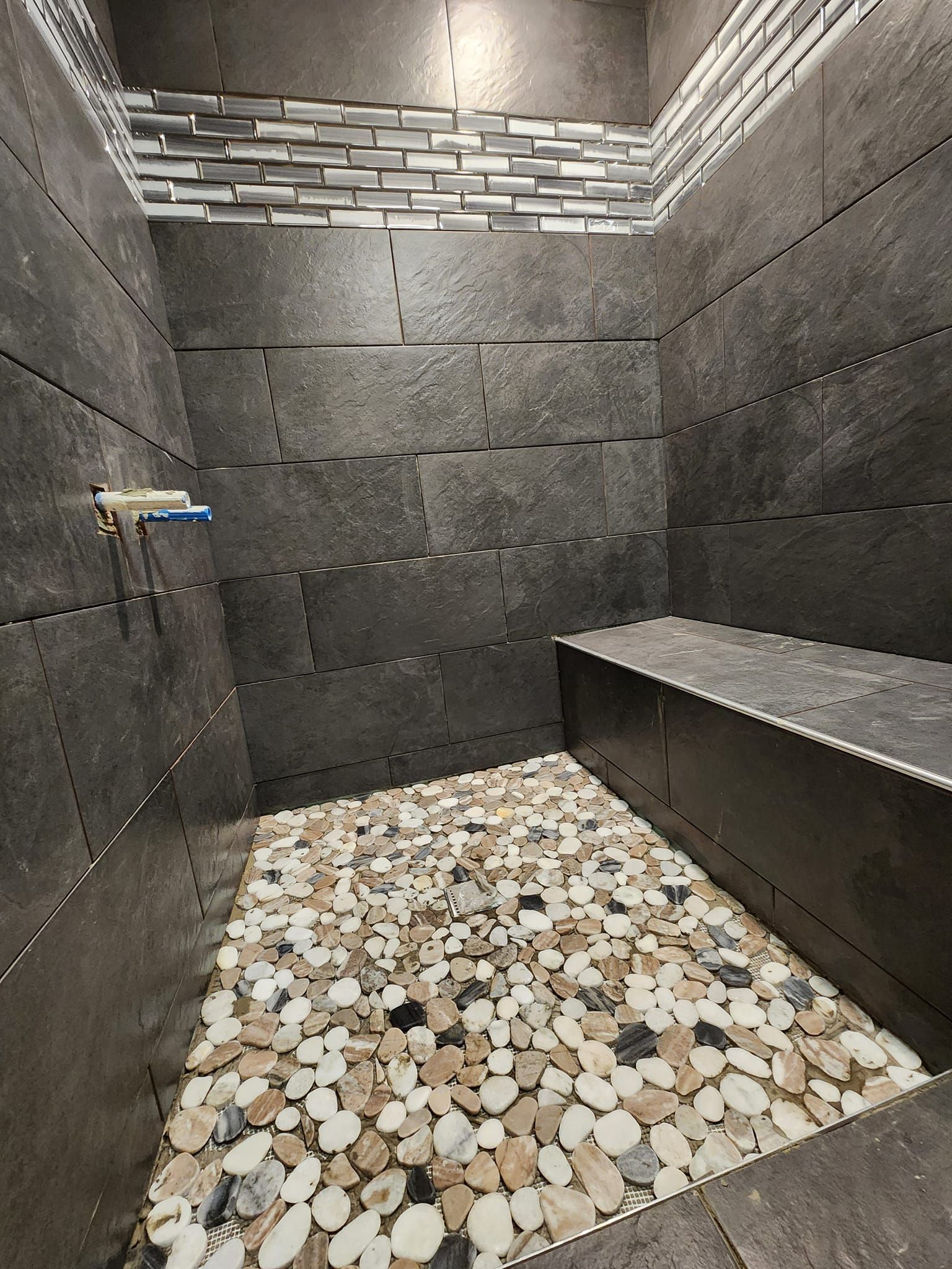 Dark gray tiled shower with pebble floor and built-in bench.