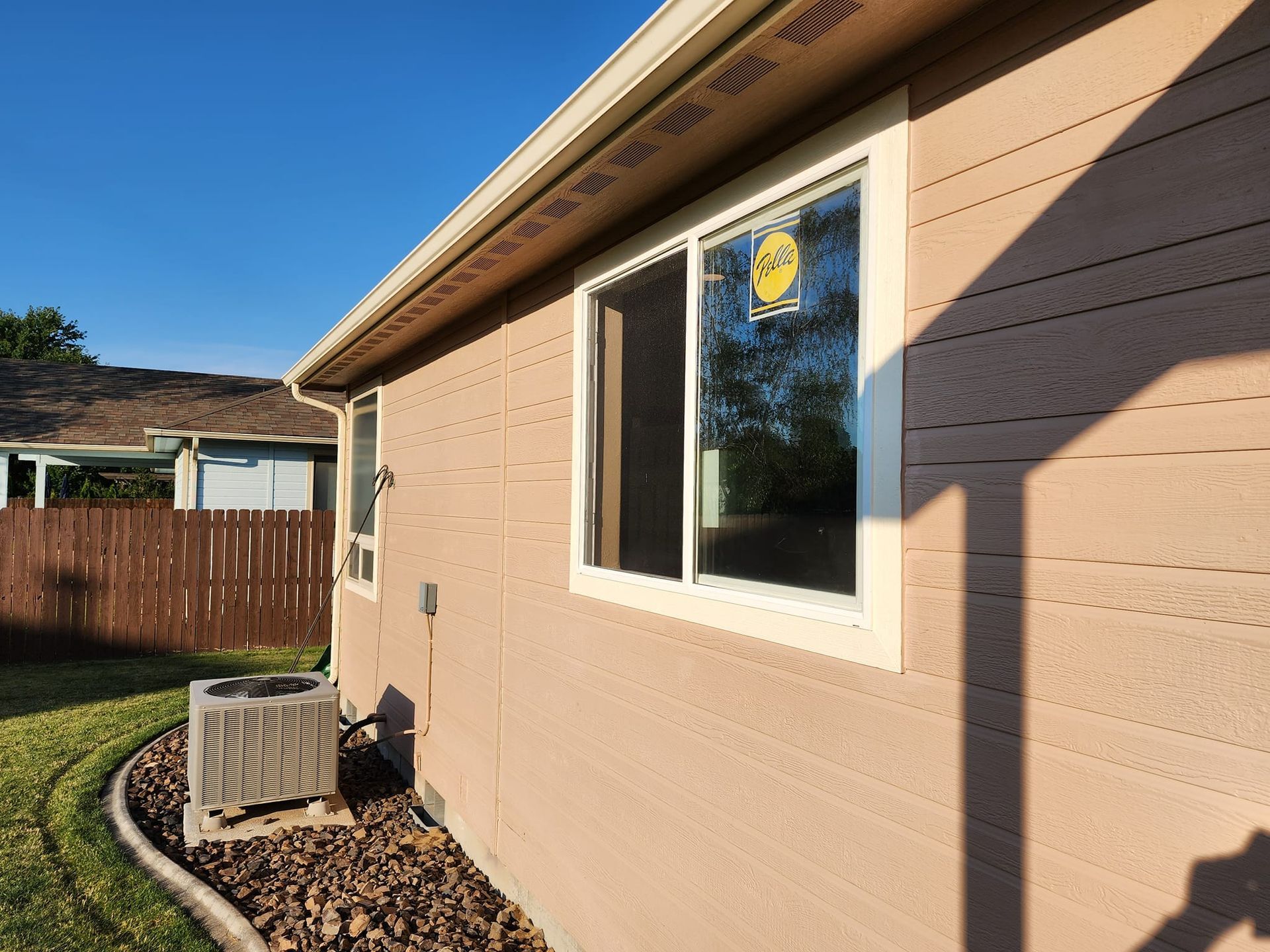 Tan house exterior with white window trim and a brown gutter, with an air conditioning unit.