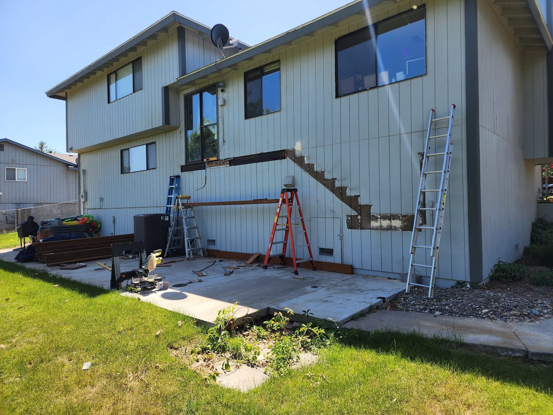 Exterior of a two-story house under construction, with ladders and exposed siding.