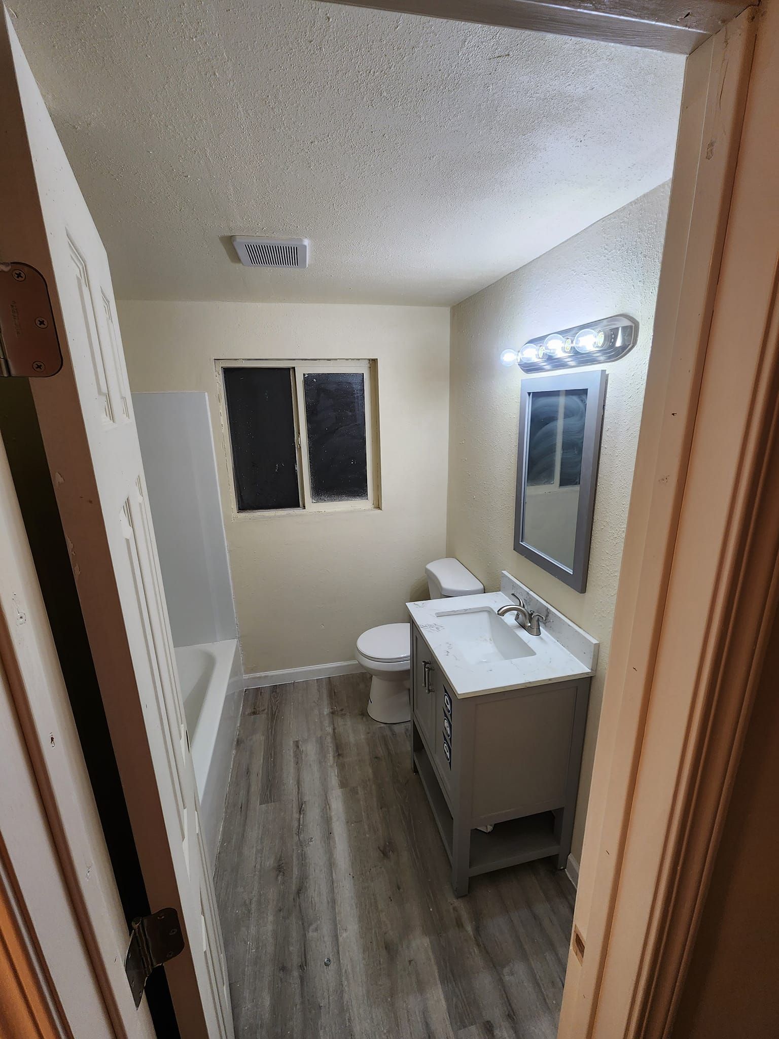 Bathroom with a bathtub, toilet, vanity, and window; gray and white color scheme.