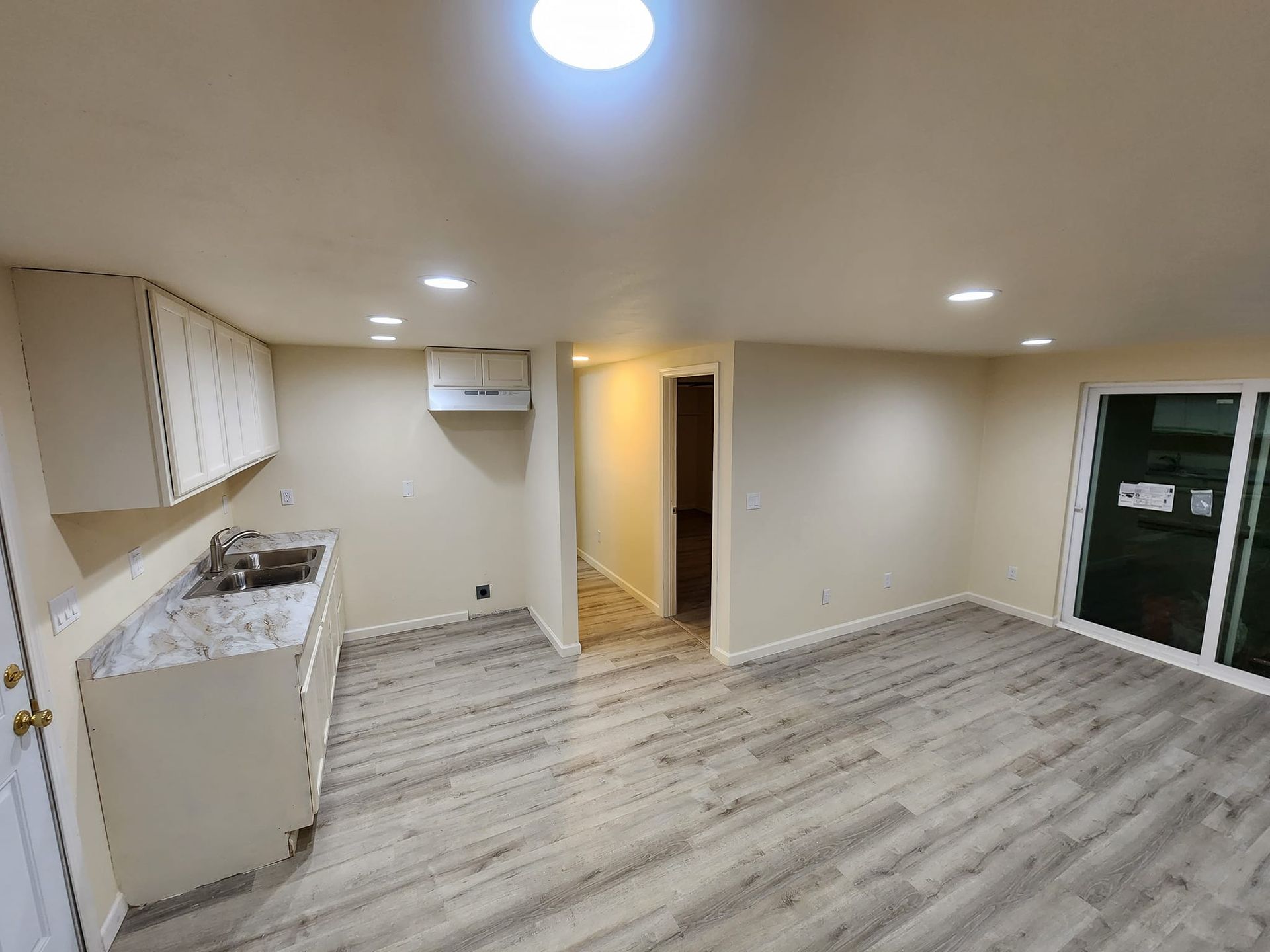 Interior view of a small kitchen area with cabinets, sink, and a doorway leading to a hallway