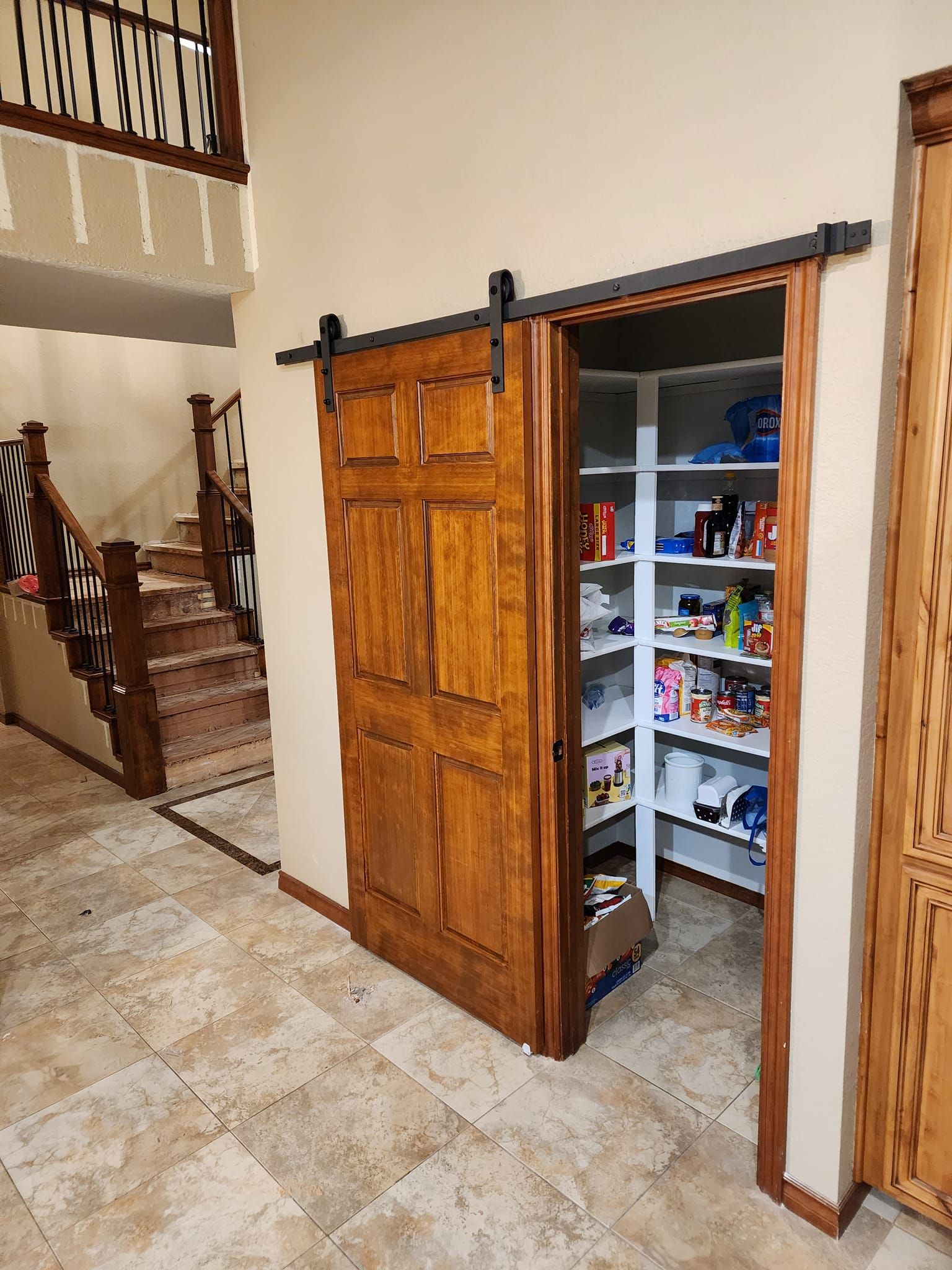Wooden barn door open to a pantry filled with food items. A staircase is in the background.