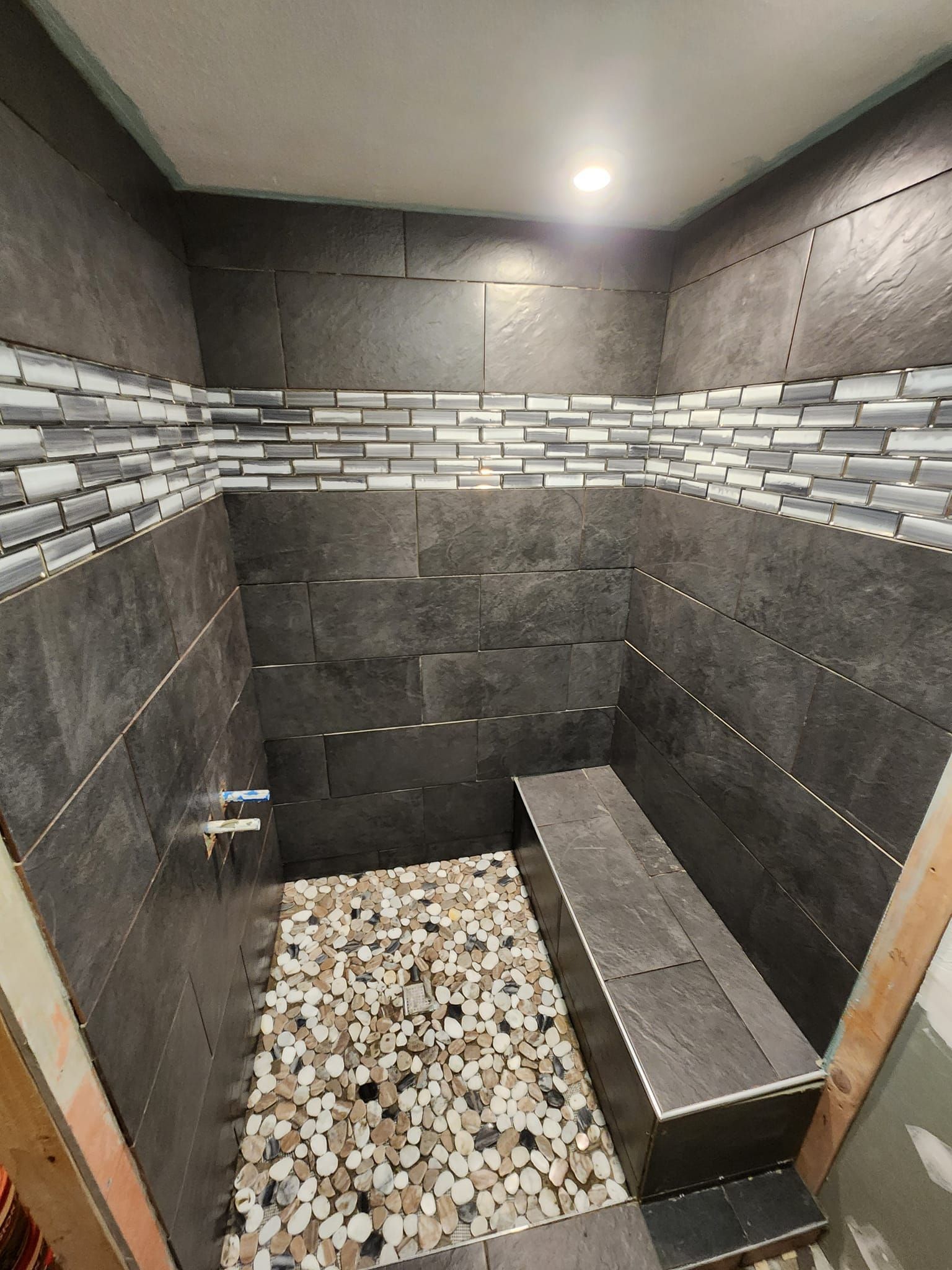 Dark tiled shower with mosaic tile stripe, pebble floor, built-in bench.