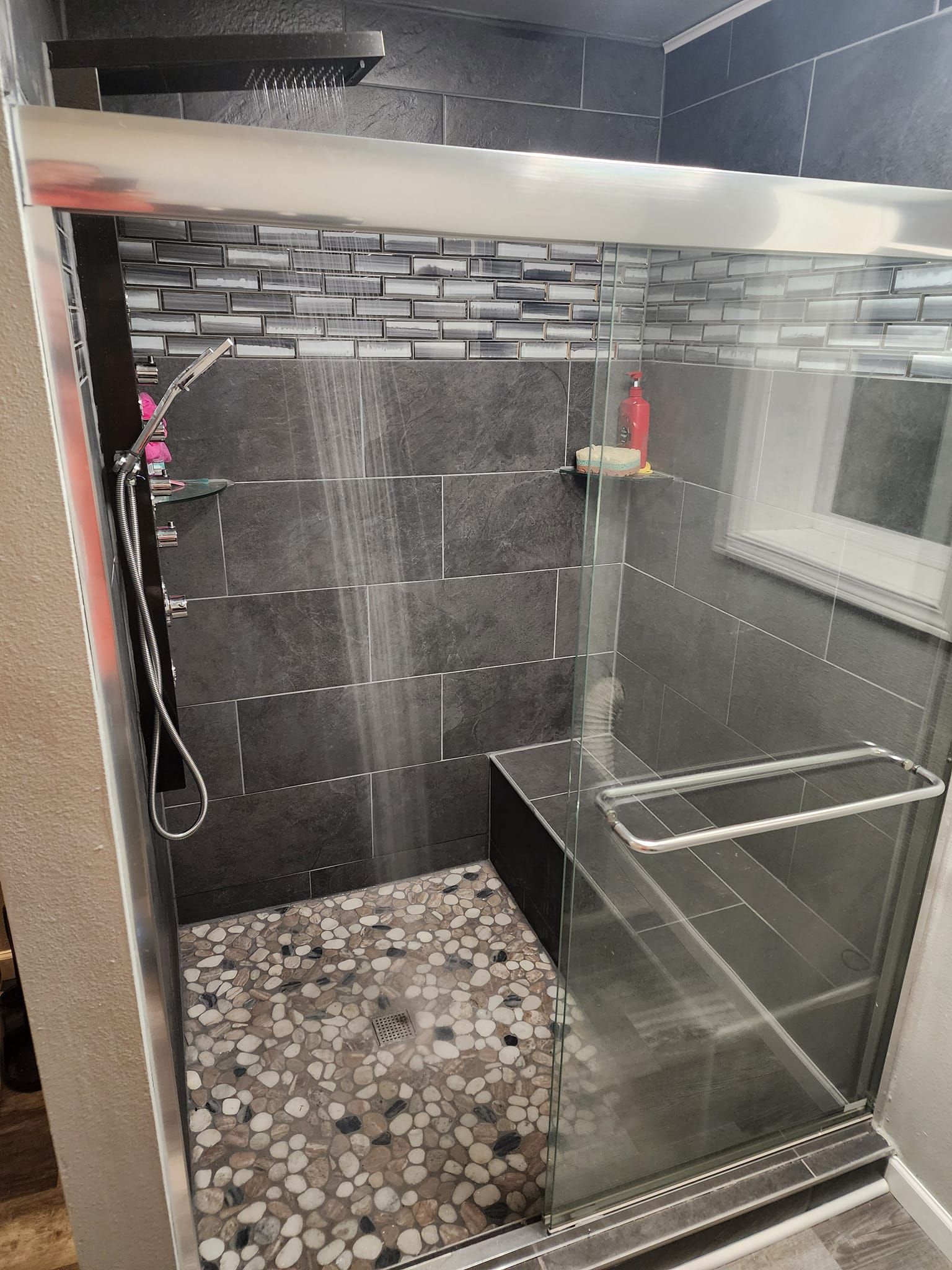 Modern tiled shower with glass door and built-in bench. Water streams from the shower head.