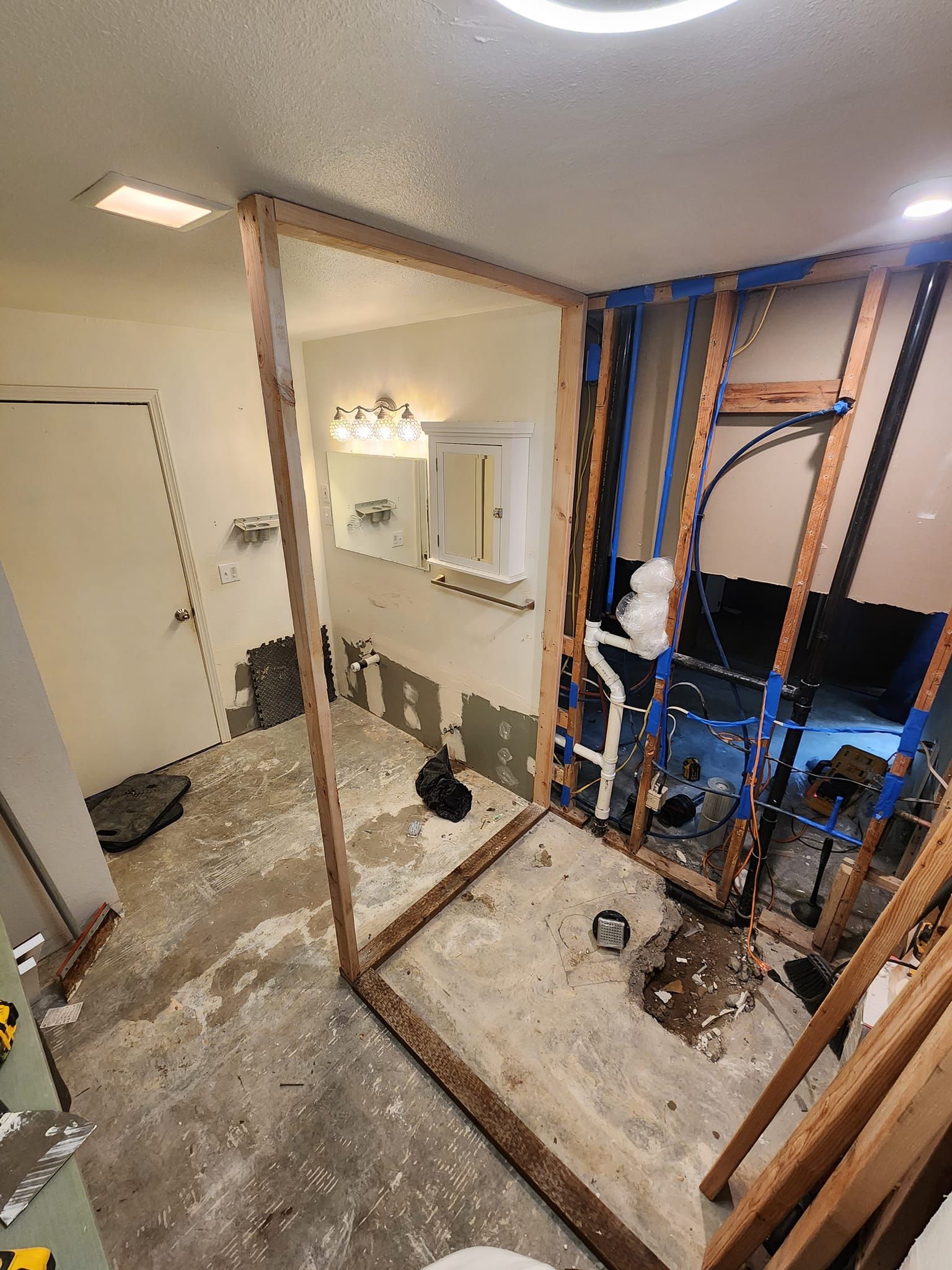 Bathroom renovation in progress; exposed studs, plumbing, and a framed shower area.