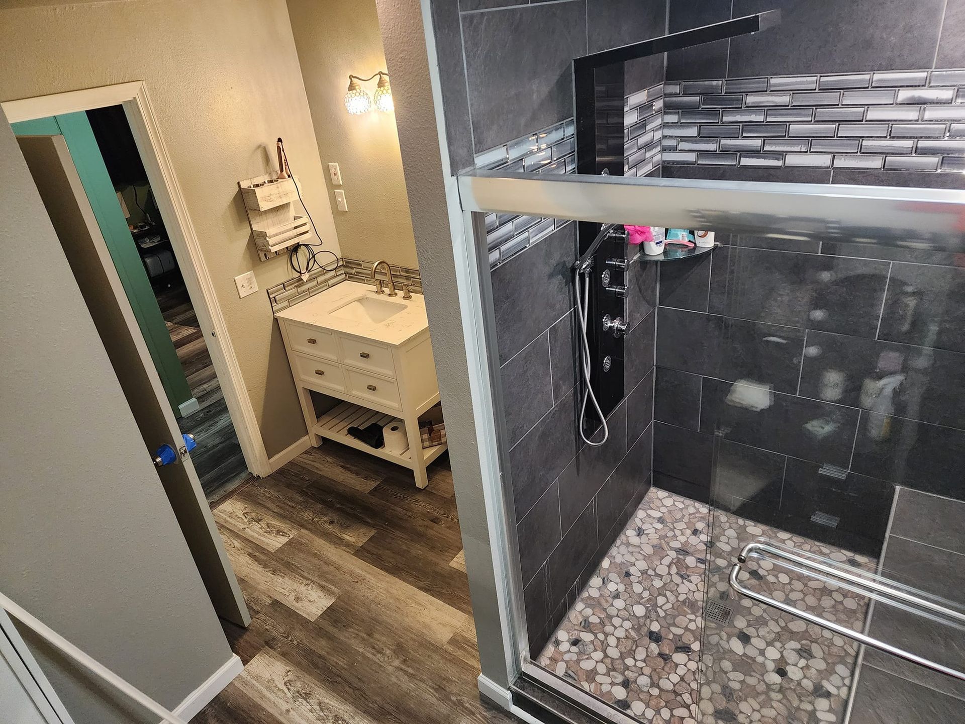Bathroom with shower, vanity, and pebble floor. Dark gray tiles and wood-look flooring.