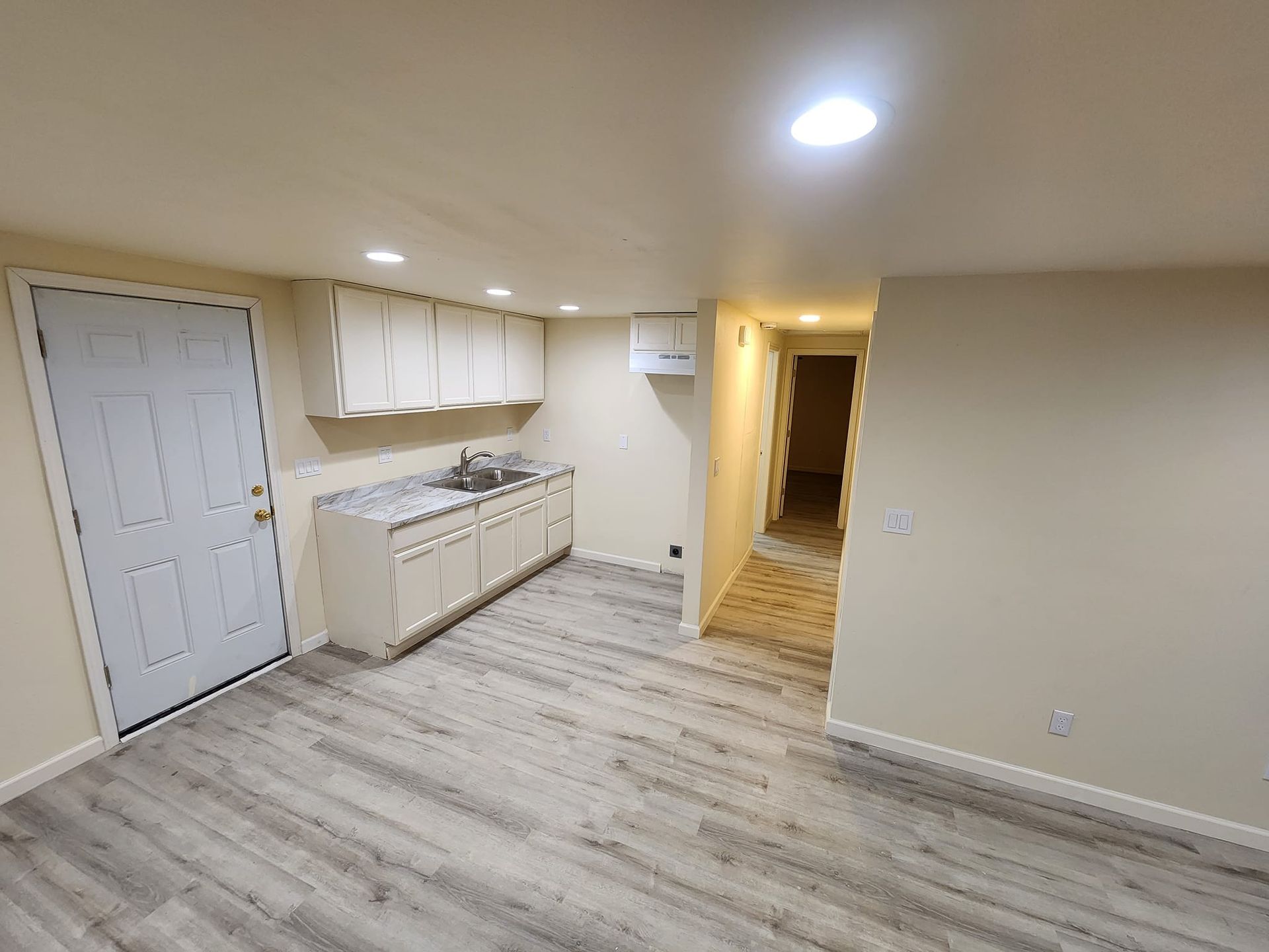 Basement room with white cabinets, sink, and a door, with gray flooring.