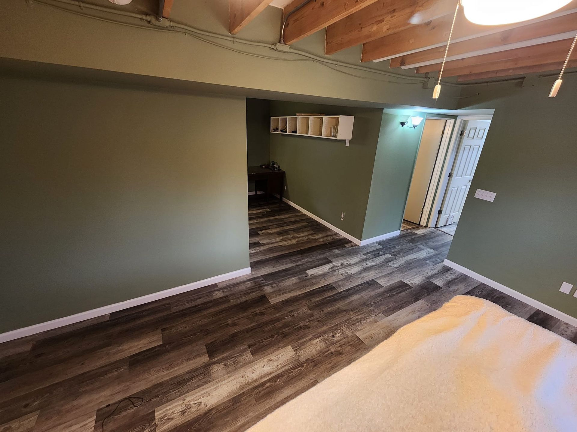 Room with green walls, wood-look floor, and white trim. Open doorway leads to more space.