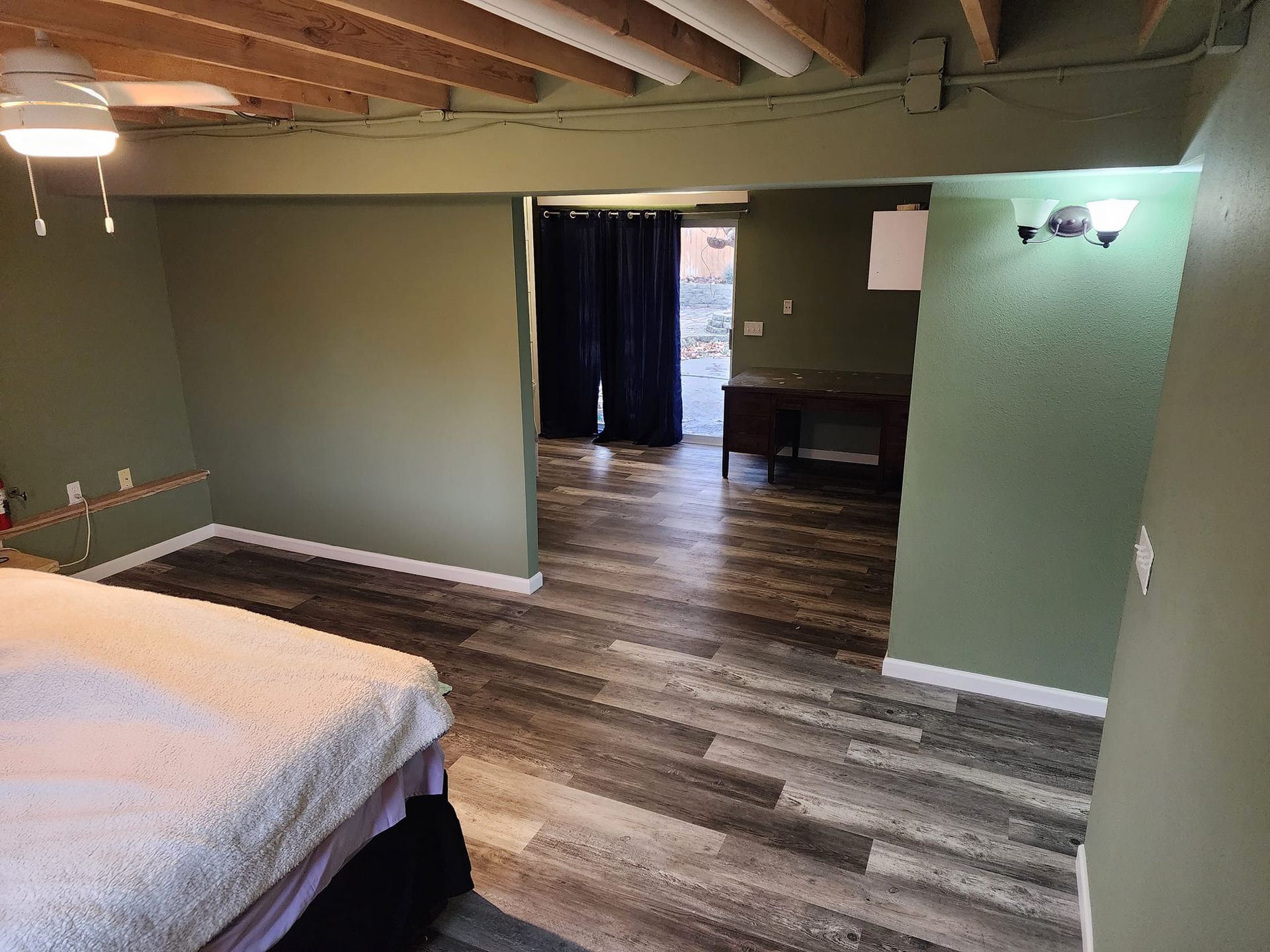 Bedroom with green walls, wood-look floor, bed, and an open doorway to another room.