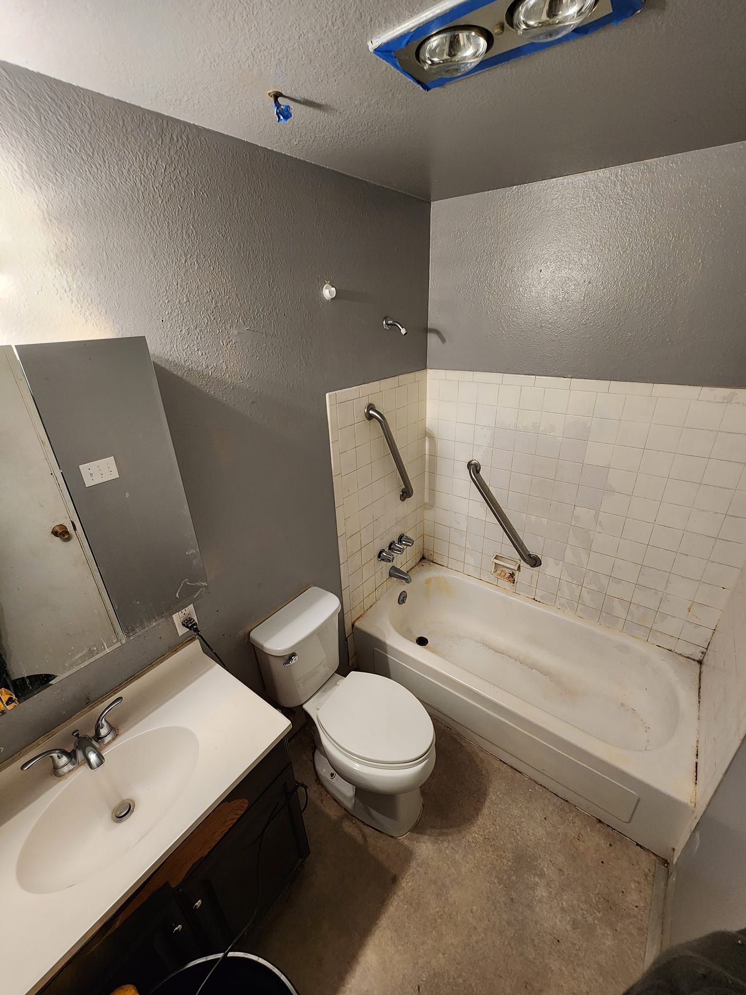 Bathroom with a sink, toilet, tub, and overhead light fixture; gray walls.