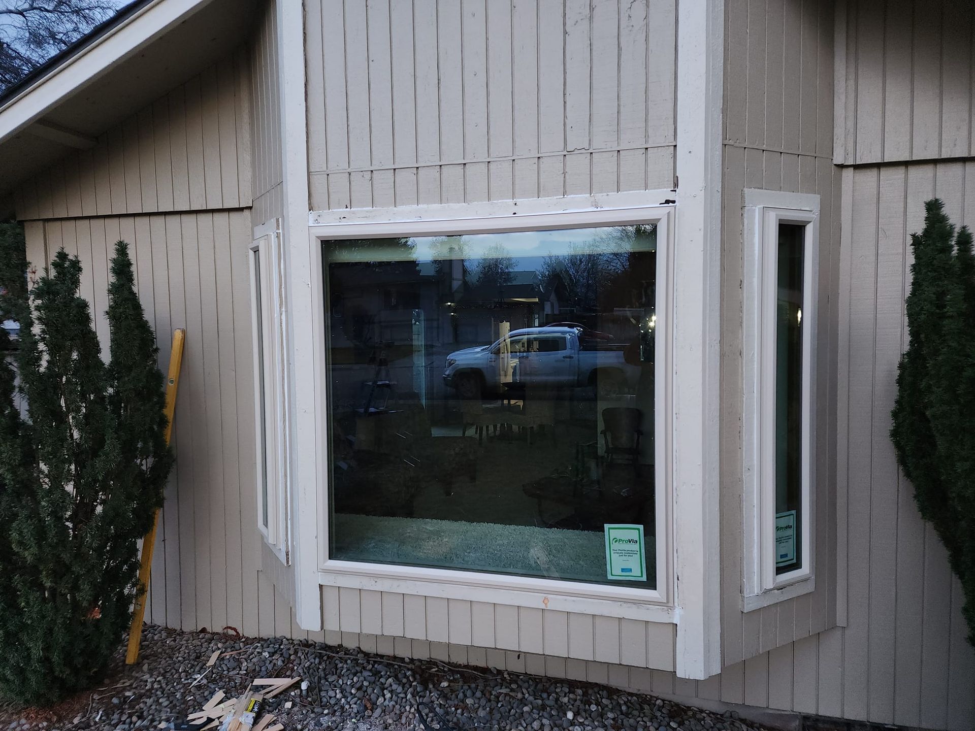 Bay window on a beige house, reflecting a car on the street, framed by white trim.