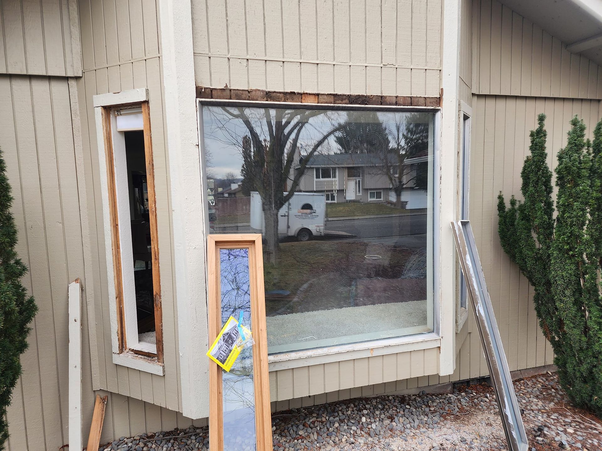 Exterior of a house with two windows, one being replaced. A large tree is reflected in the remaining window.