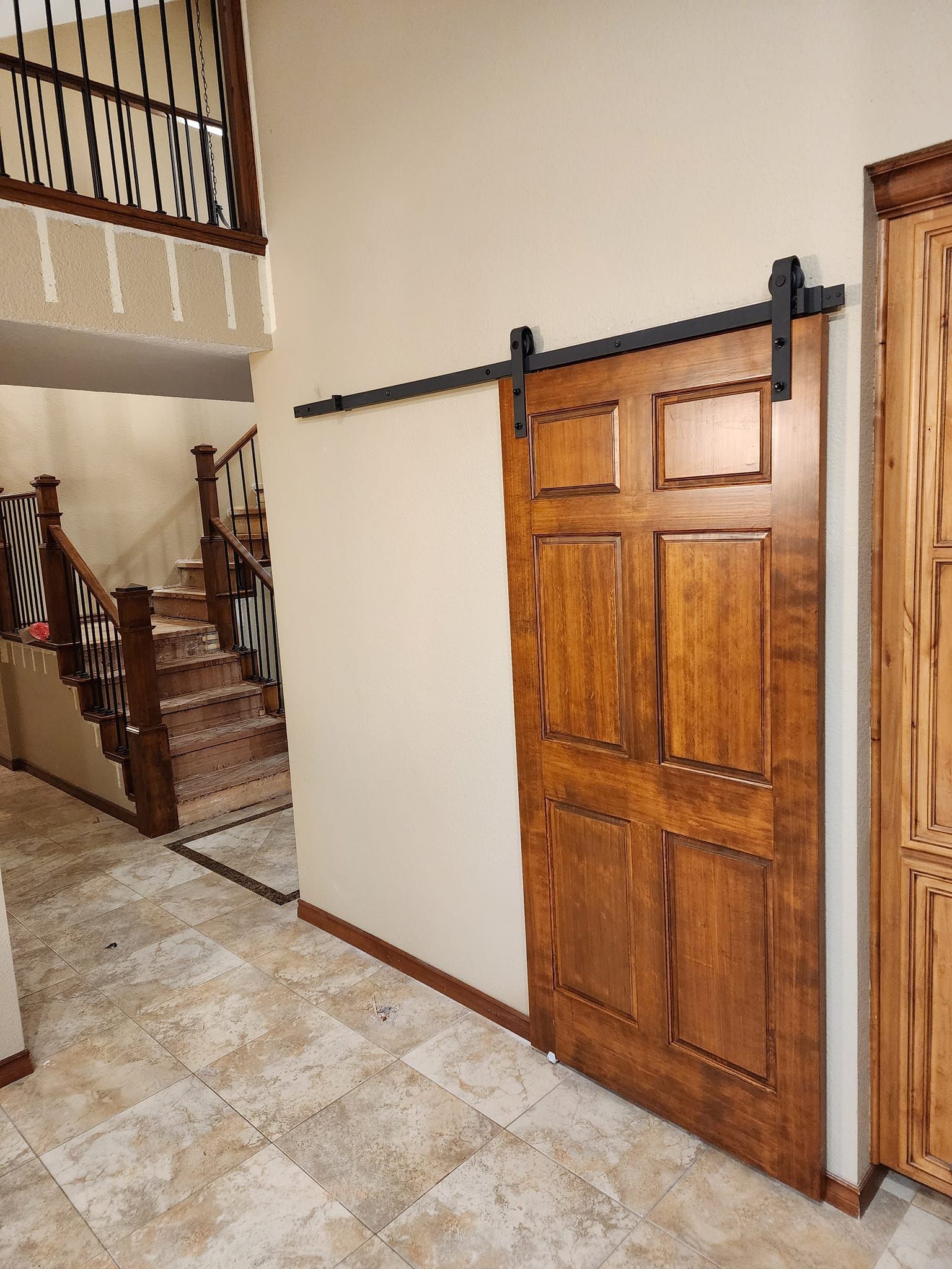 Wooden sliding barn door on tan wall, black hardware. Staircase and hallway visible.