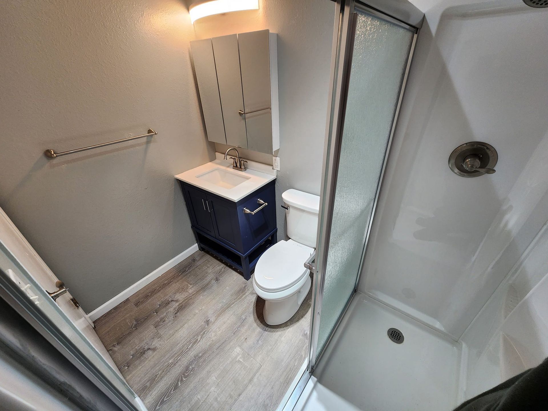 Bathroom with gray walls, blue vanity, toilet, and shower with glass door.