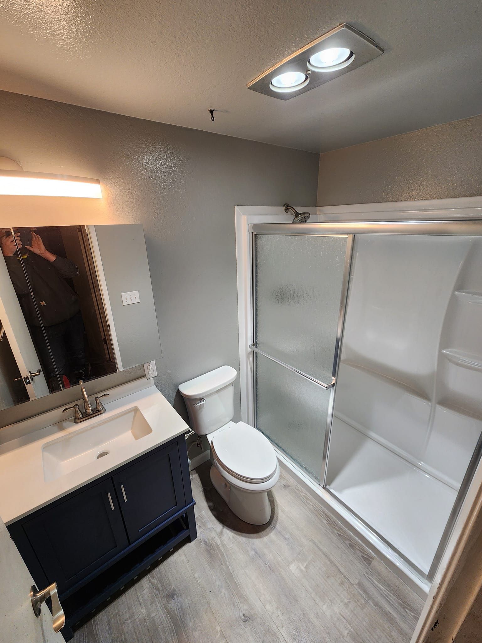 Bathroom with a dark blue vanity, toilet, and shower with frosted glass doors; gray walls.