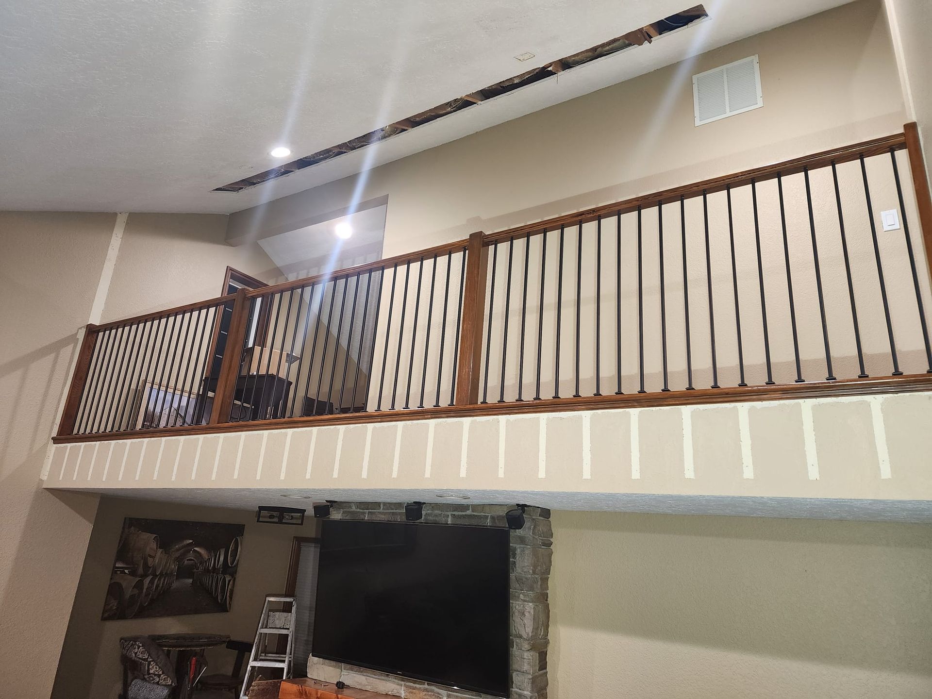 Loft with dark wood railing and vertical bars overlooking a living room with a stone fireplace and TV.