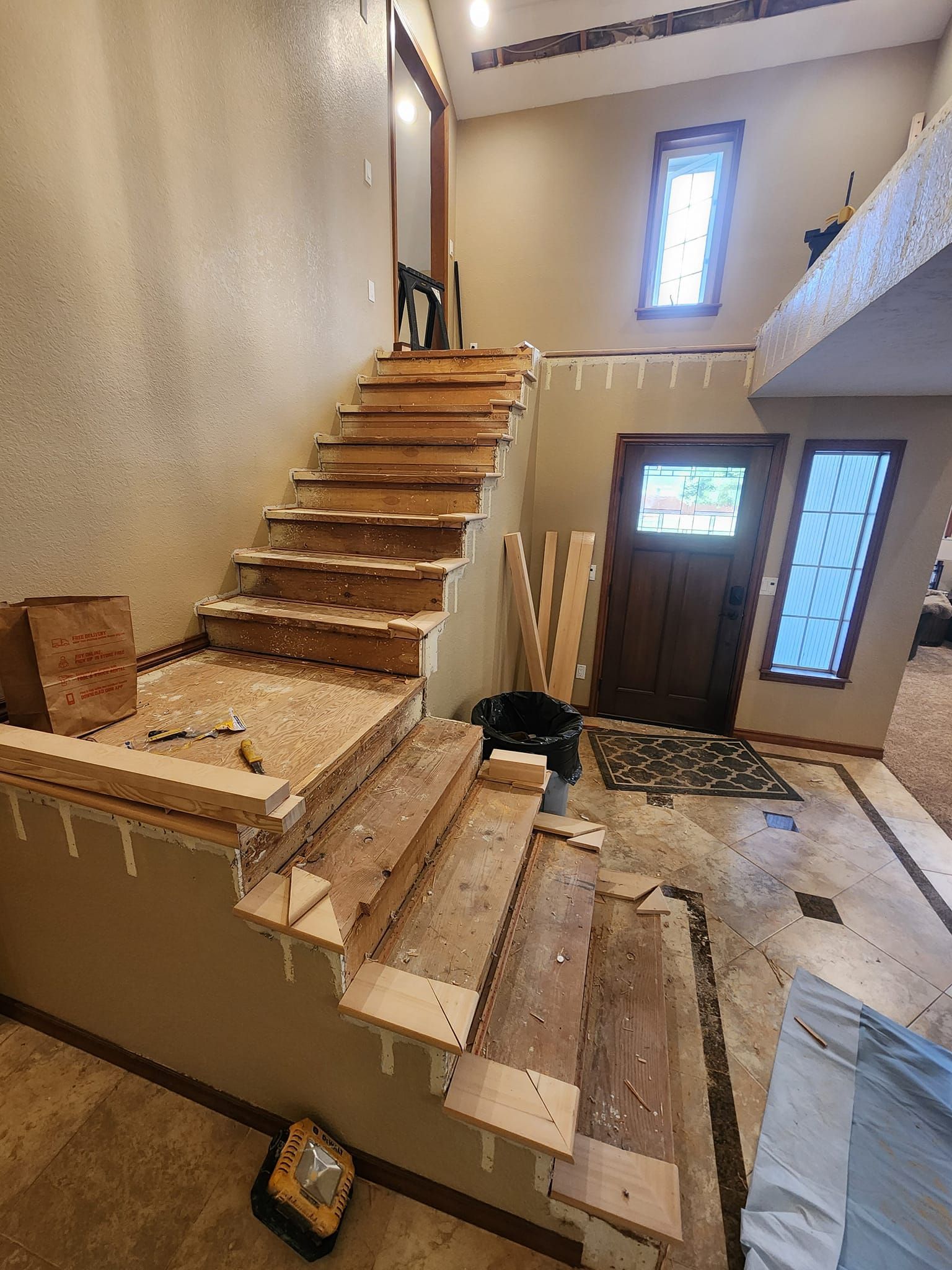 Staircase under construction, exposed wooden steps, doorway with window, beige walls, indoor setting.