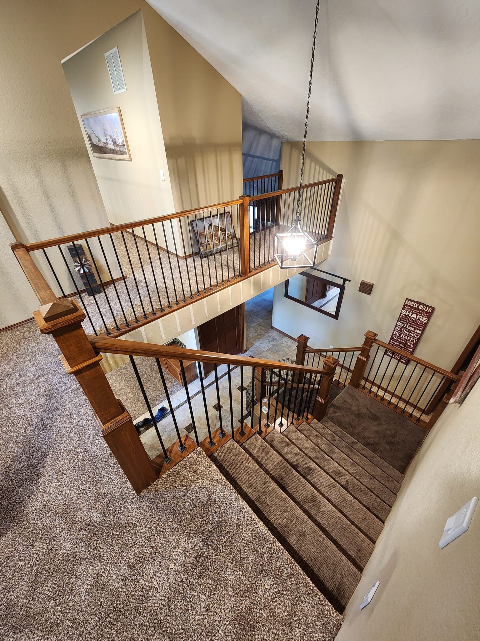 High-angle view of a two-story staircase with brown carpet, wooden railings, and black spindles.