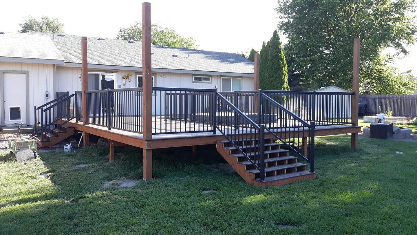 Wooden deck with brown and black railings and stairs in a backyard.