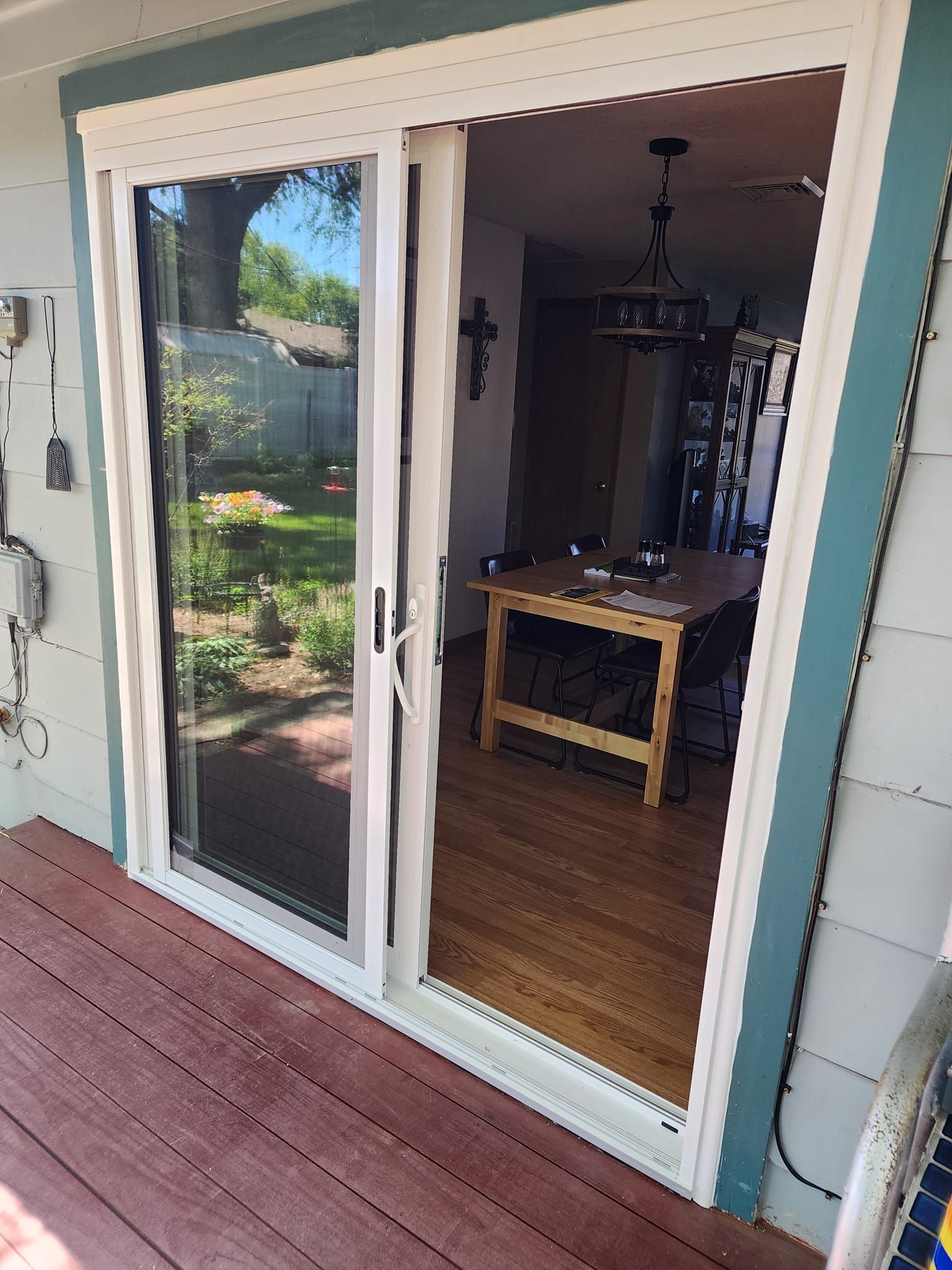 Sliding glass door, open to interior with wooden table and chairs. Exterior shows garden and deck.
