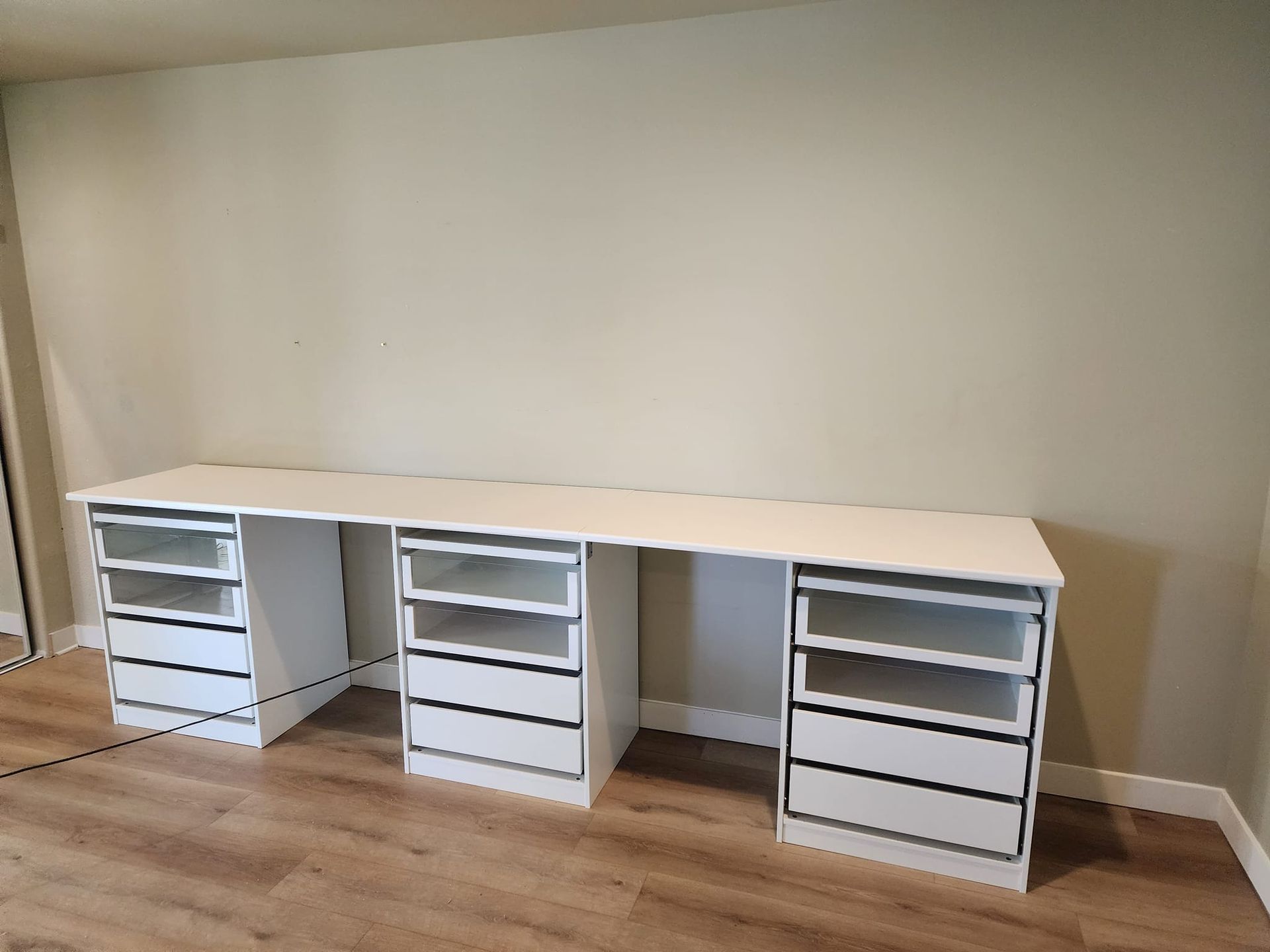 White desk with multiple drawers against a light beige wall. Wooden floor.