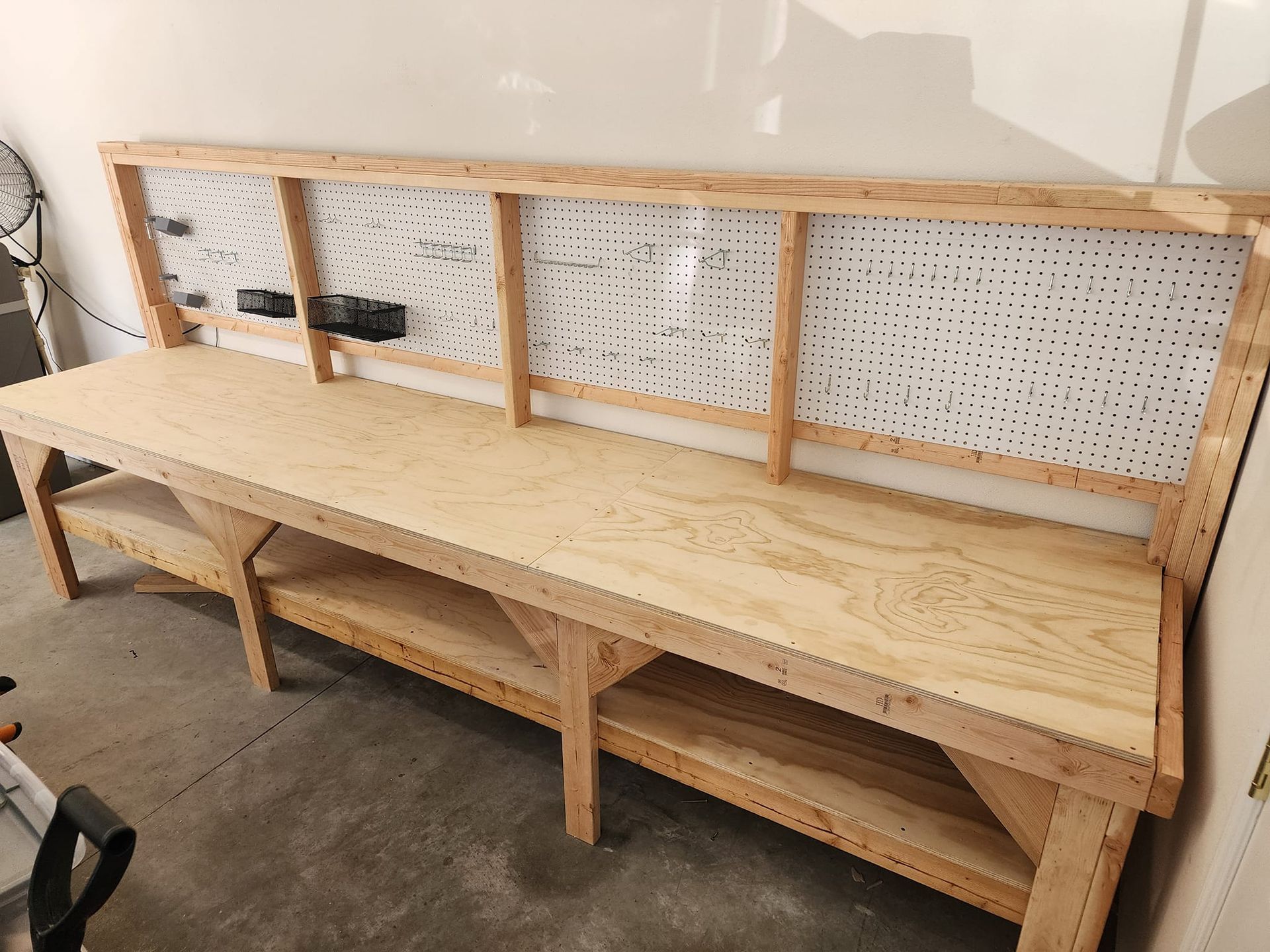 Wooden workbench with pegboard backing, mounted against a wall in a garage.