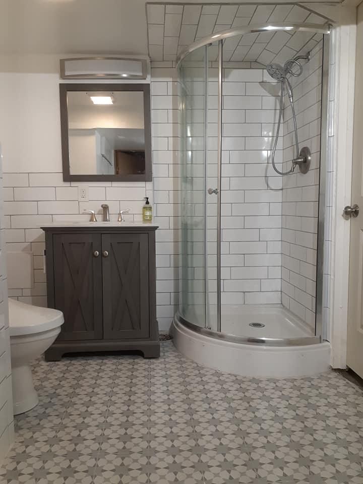 Bathroom with gray vanity, white subway tile, a curved glass shower, and patterned floor tile.