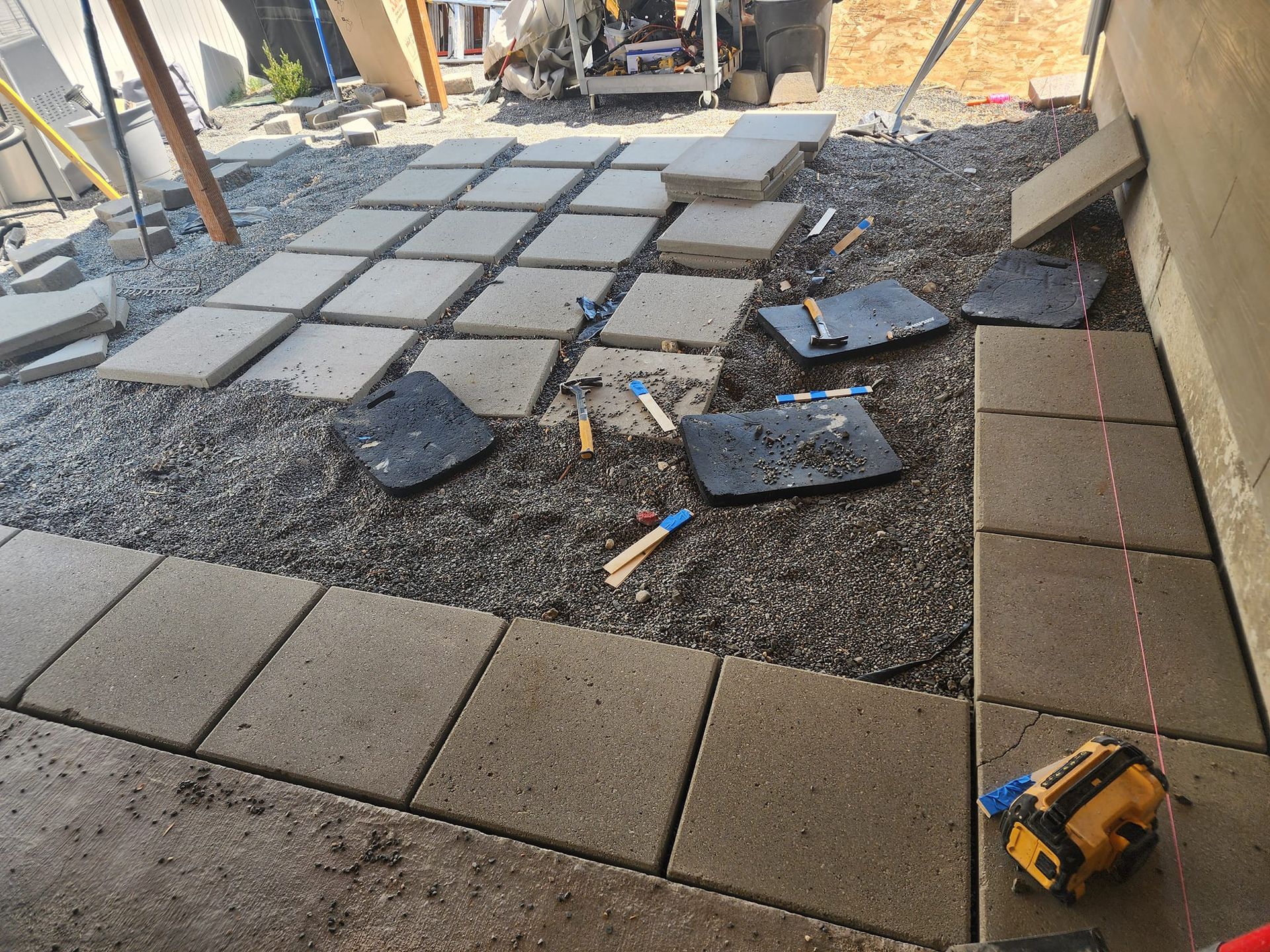 Construction site: pavers being laid on gravel base, near a building.