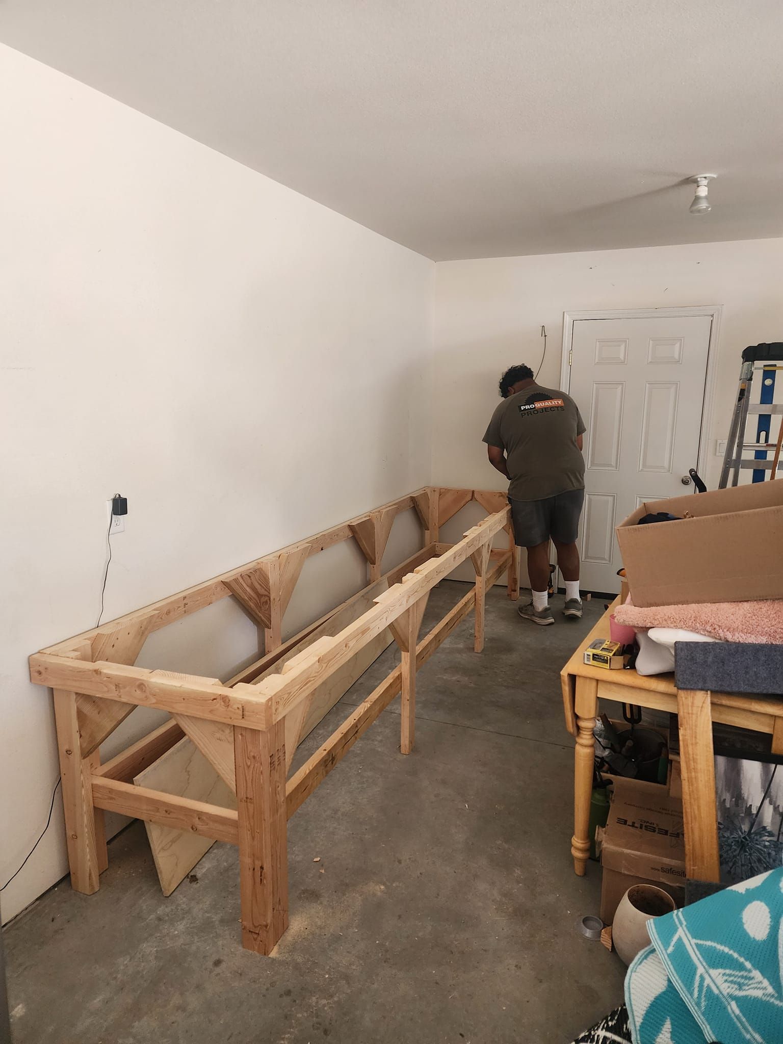Man building wooden structure in garage. Structure against white wall, near door and table.