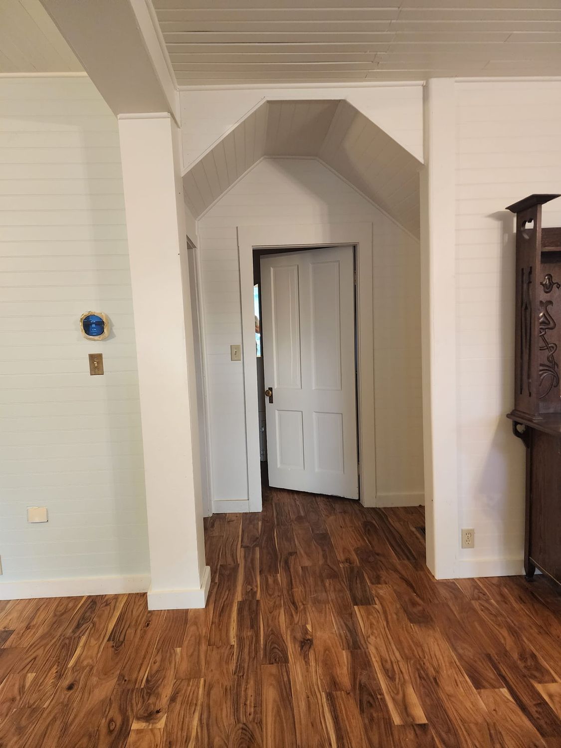 Interior view: hallway with arched ceiling, white walls, wood floor, and open white door.