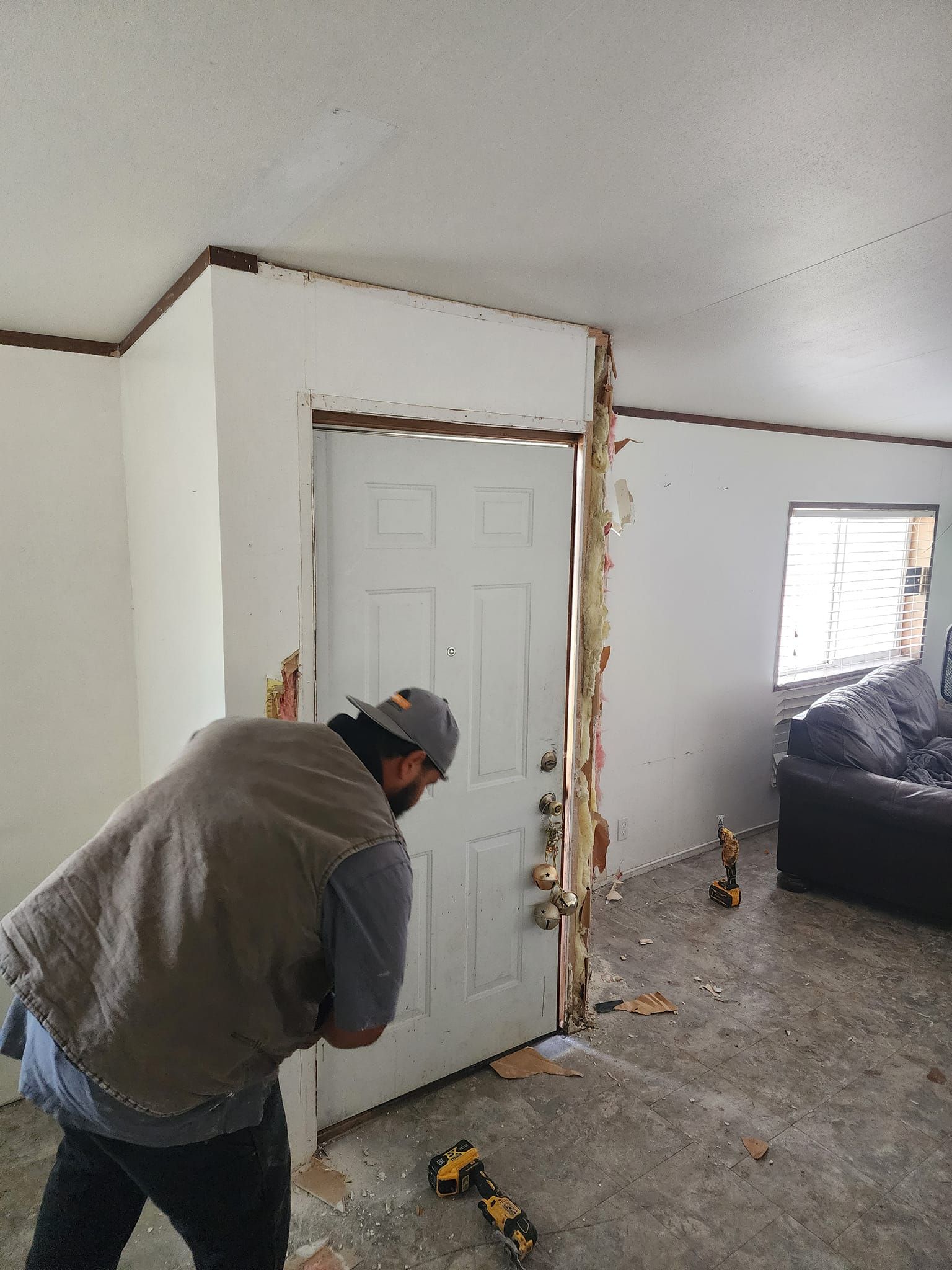 Person removing trim around a white door in a room with damaged walls and debris on the floor.