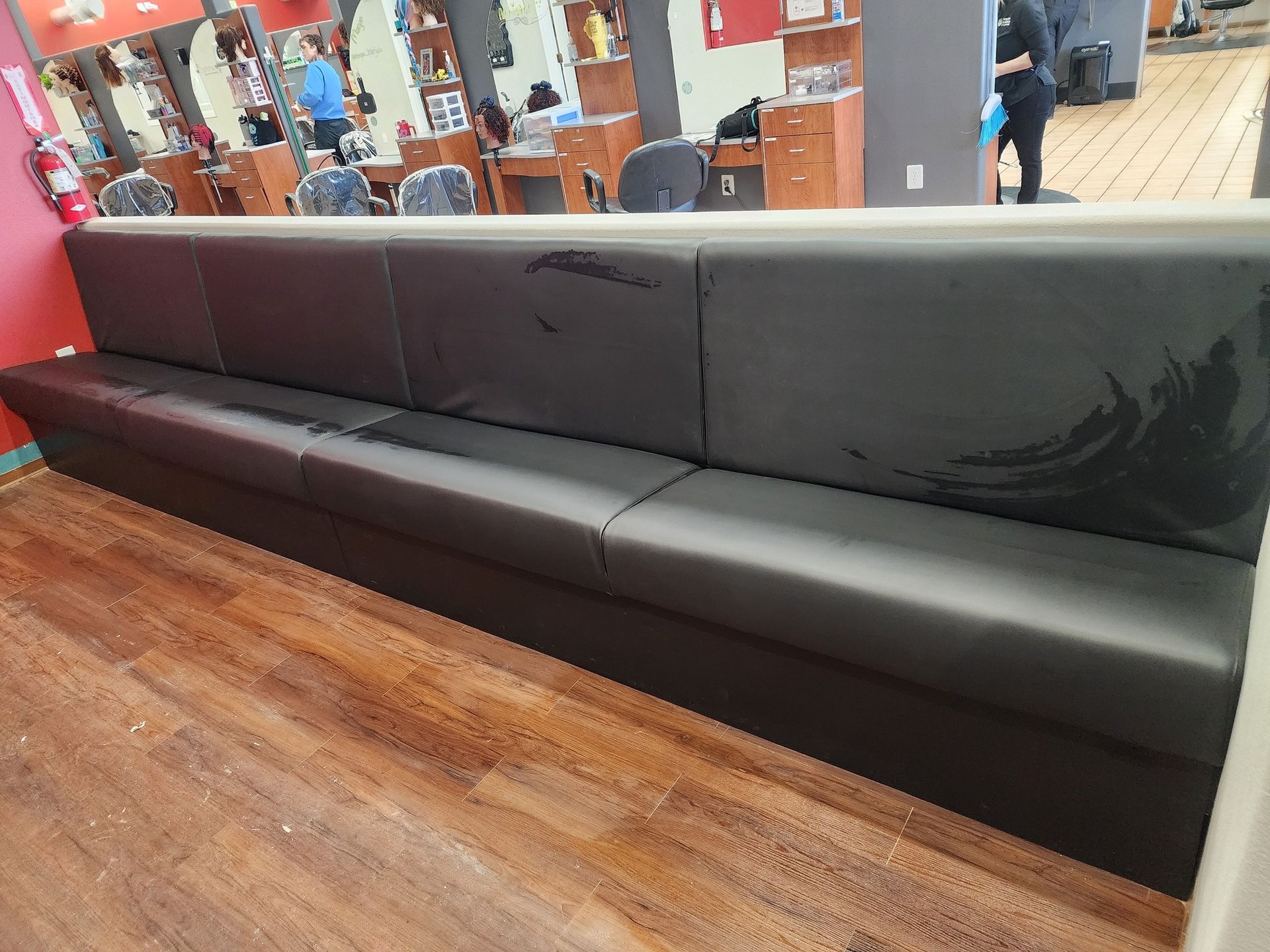 Long black bench in a barber shop, with visible wear and tear. Wooden floor and red wall.