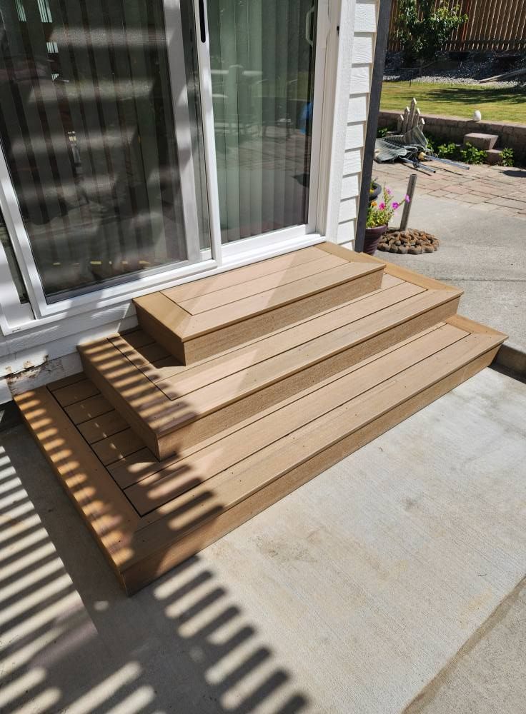 Three-step deck with light brown boards leading to a sliding glass door. The deck sits on concrete.