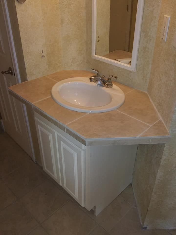 Bathroom vanity with white cabinet, tiled countertop, and oval sink. Mirror above.