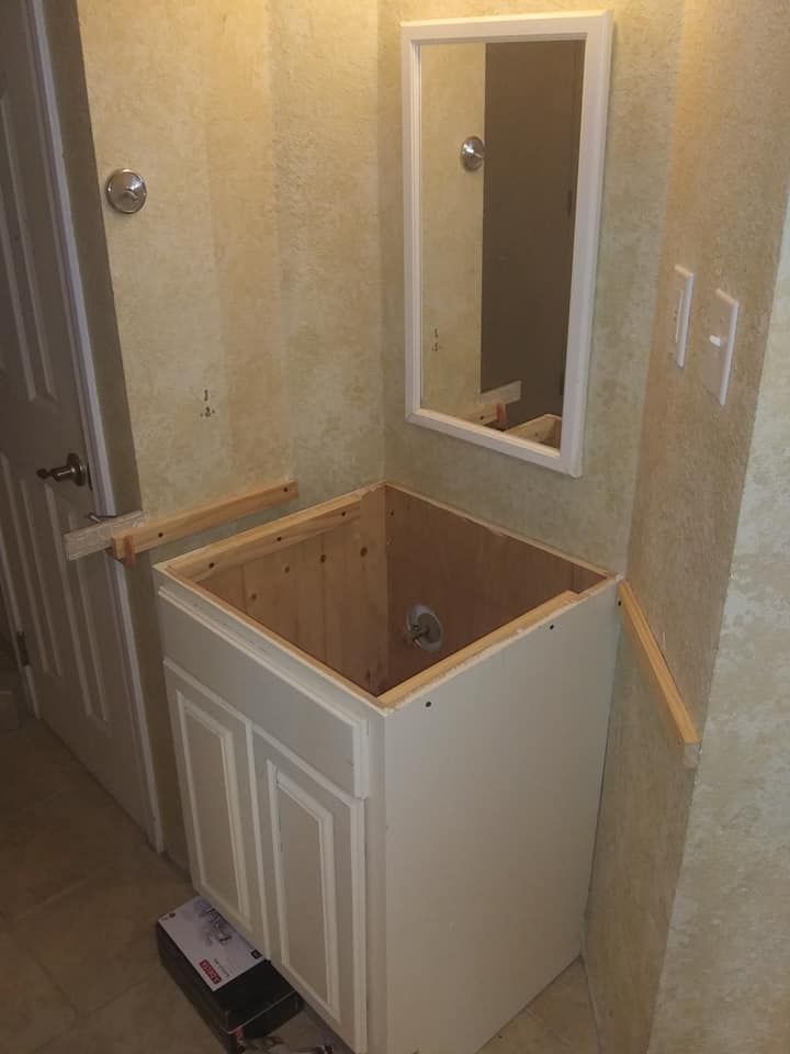 Bathroom with a white vanity cabinet, mirror, and partially installed trim.