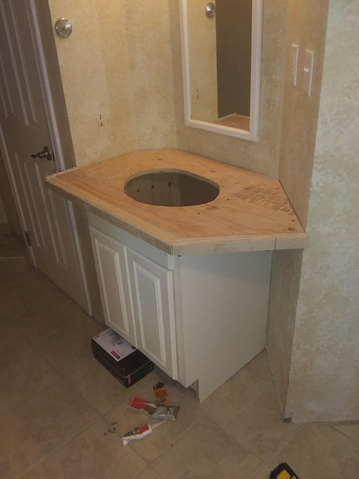 Bathroom vanity with wooden countertop, white cabinet, and mirror. Construction tools and materials present.