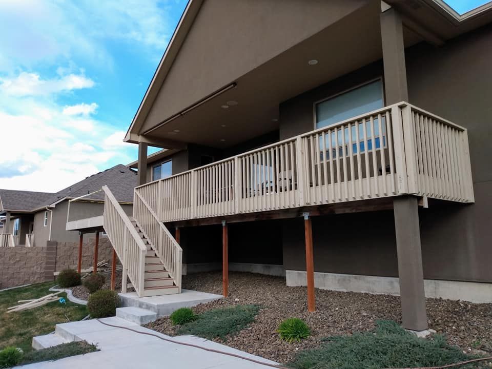 A two-story house with a wooden deck and stairs. Beige deck and railings, brown support posts, and brown siding.
