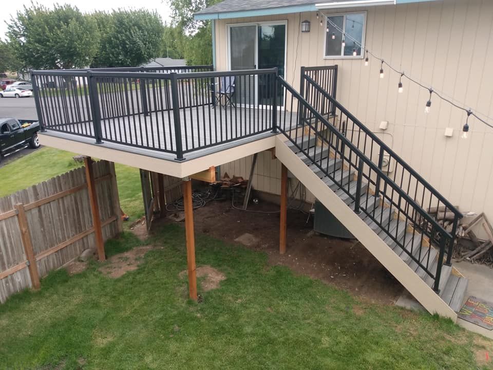 Black railing deck with stairs attached to a light-colored house. String lights hang above.