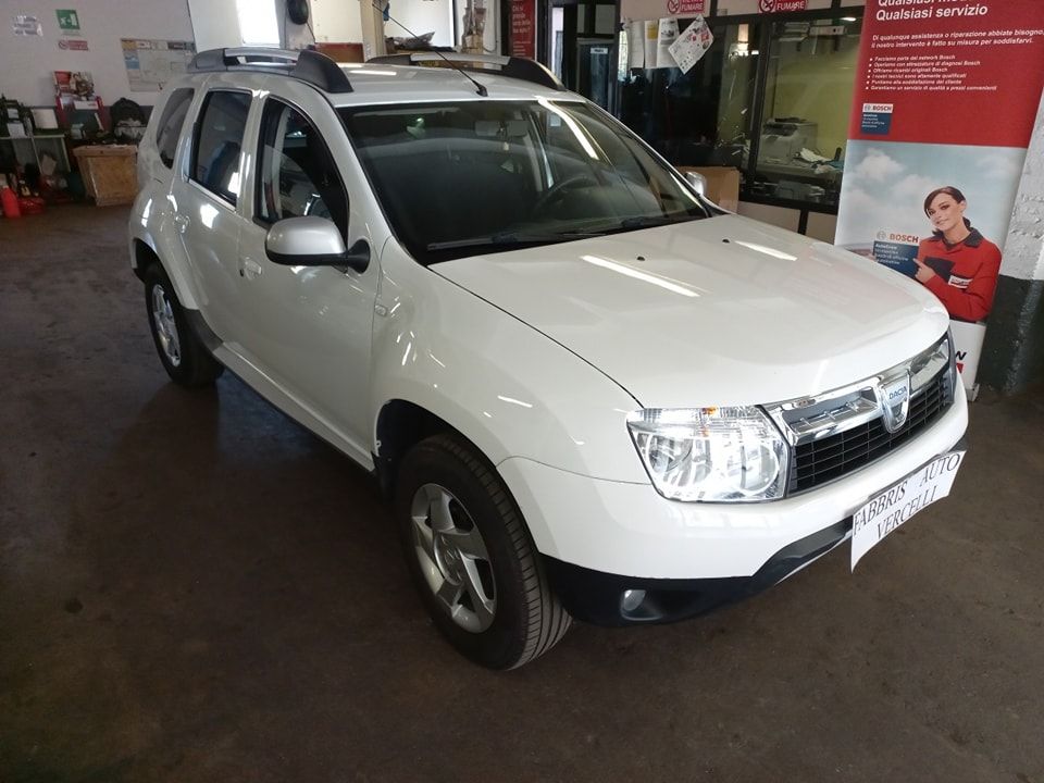 SUV bianco parcheggiato all'interno di un'officina, vista frontale con un'altra auto sullo sfondo.
