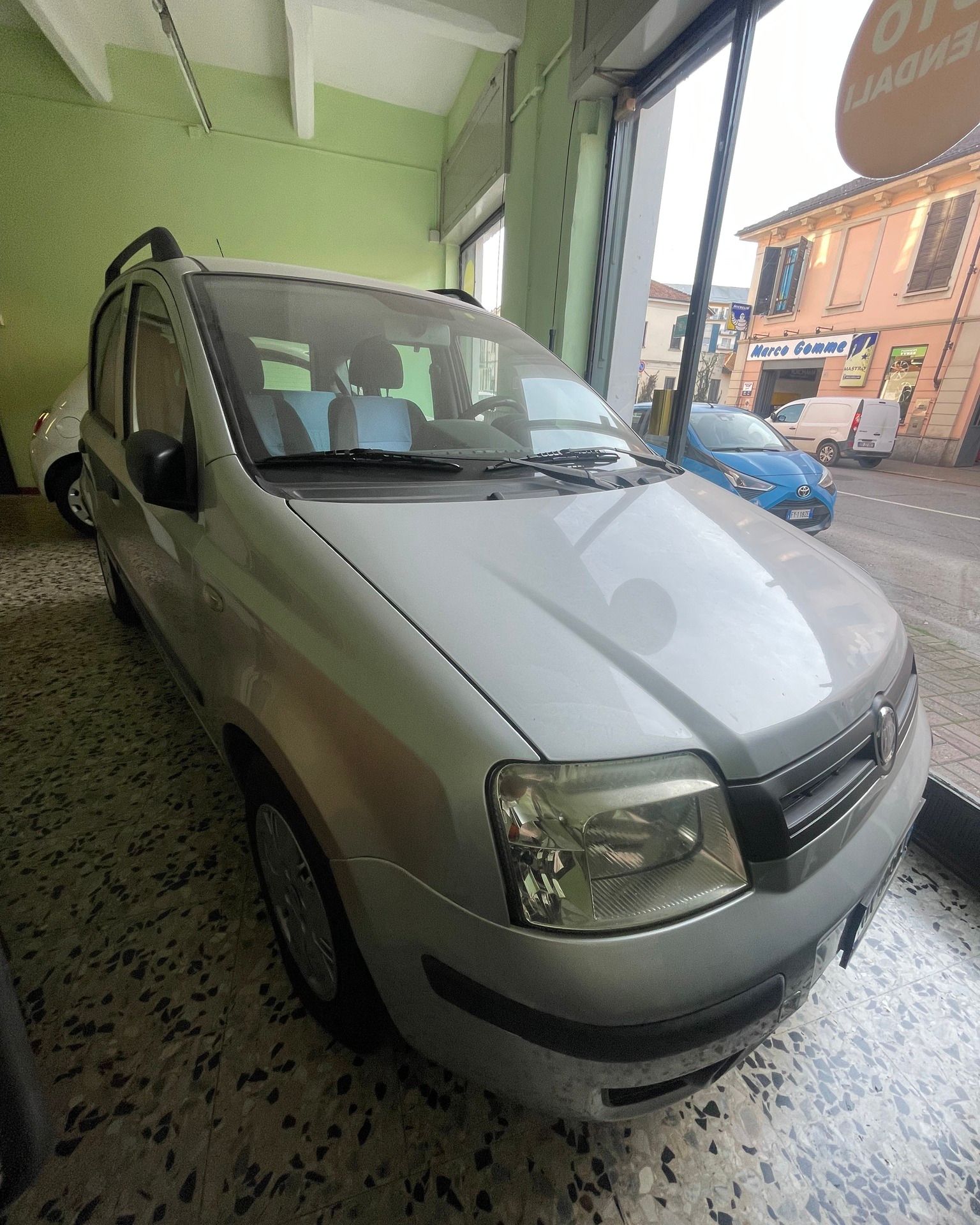 Furgone compatto color argento parcheggiato all'interno di un negozio, vicino alla vetrina, rivolto verso la strada.