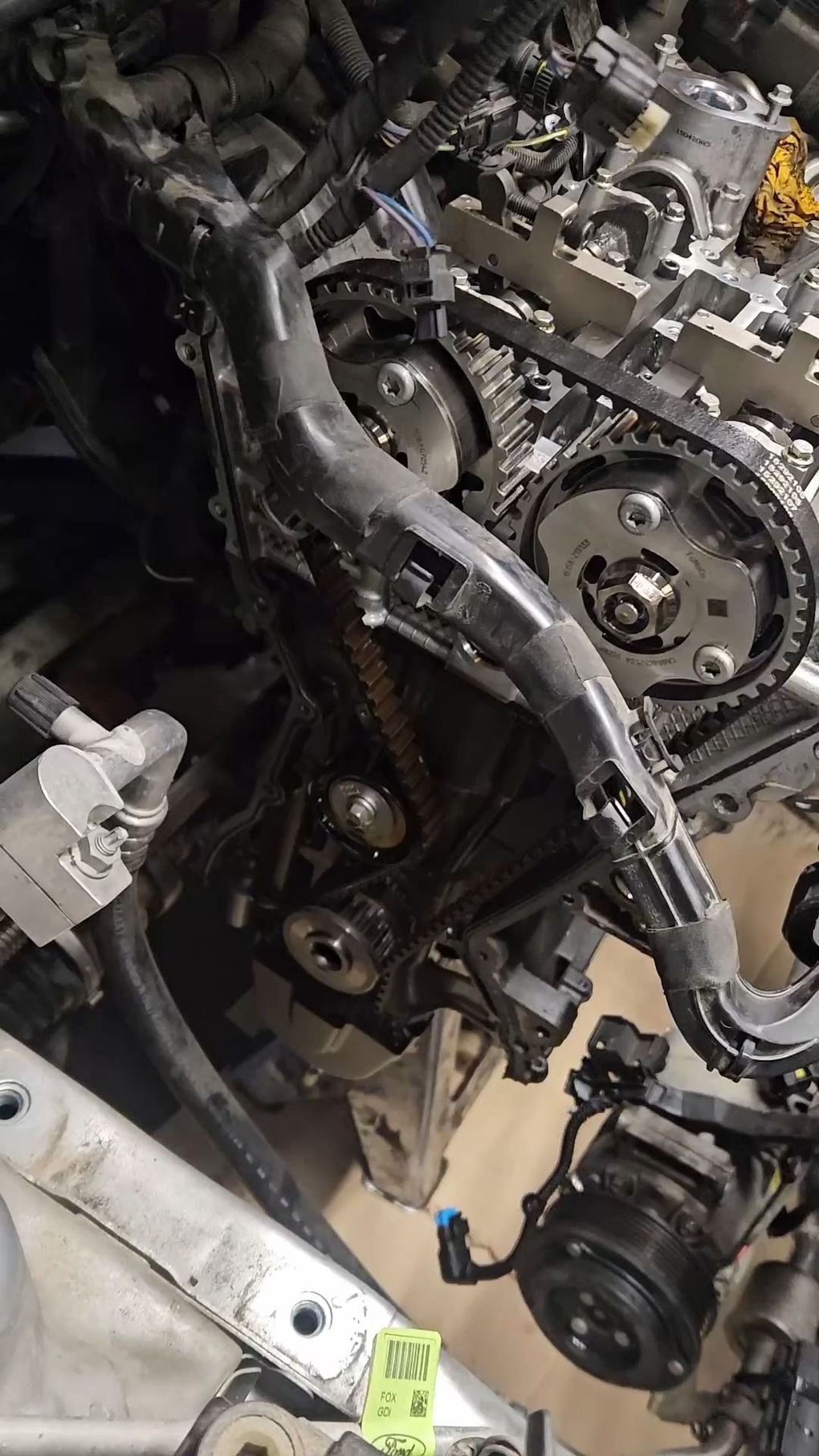 Primo piano di un motore d'auto con catena di distribuzione, cinghie e componenti metallici a vista in un garage.