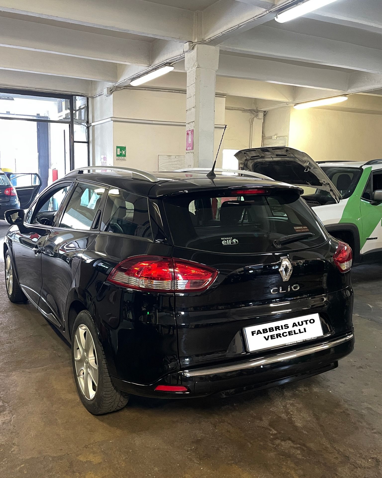 Una berlina nera parcheggiata in un garage coperto accanto ad altre auto sotto luci fluorescenti.