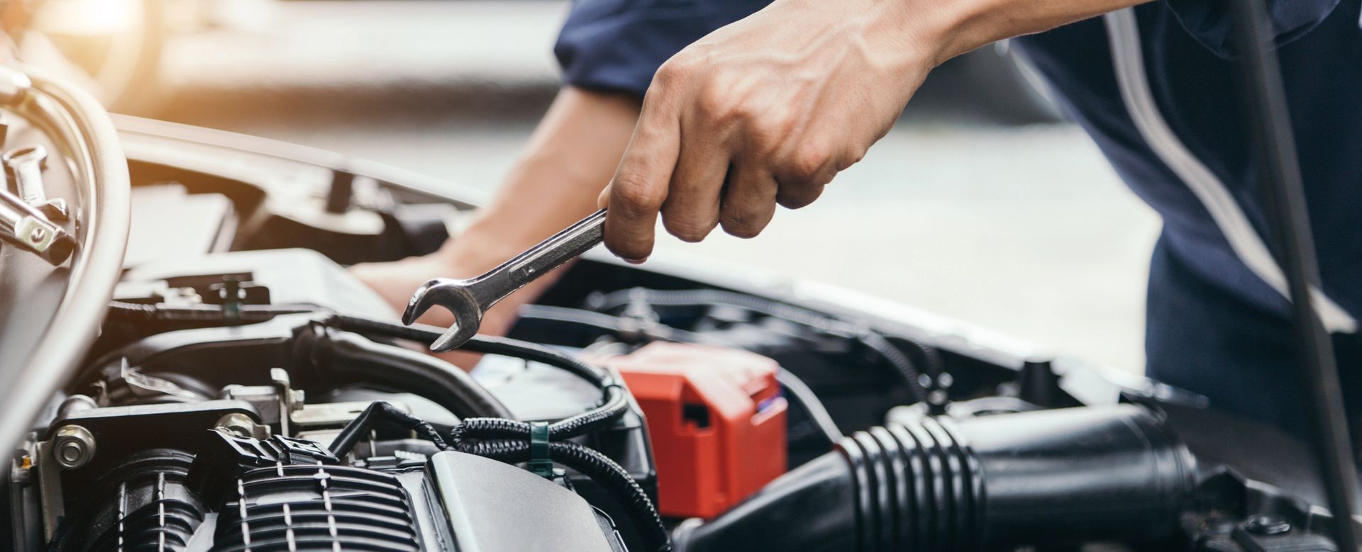 Un meccanico usa una chiave inglese per ispezionare il motore di un'auto sotto il cofano.