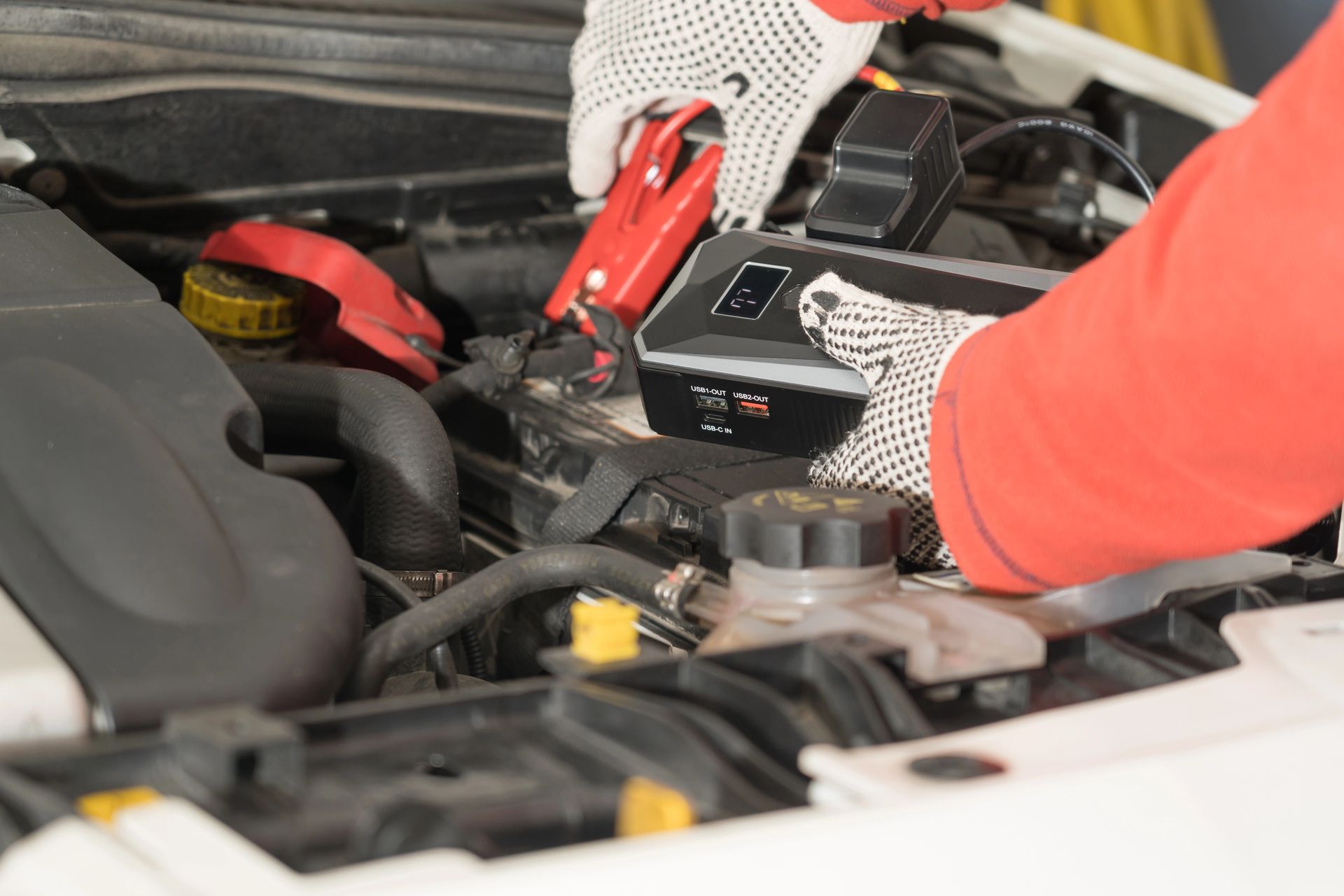 Mani guantate che usano i cavi di avviamento per collegare la batteria di un'auto nel vano motore.