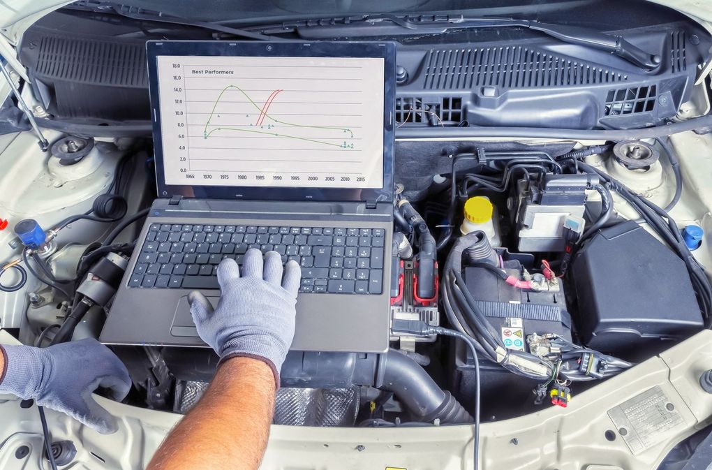 Un meccanico utilizza un computer portatile per diagnosticare un problema al motore di un'auto sotto il cofano aperto.