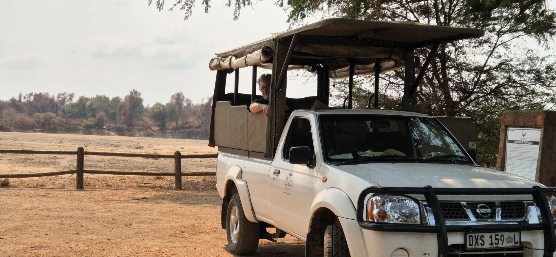 White safari truck with an open roof in a dry, grassy landscape. A person is visible in the truck.