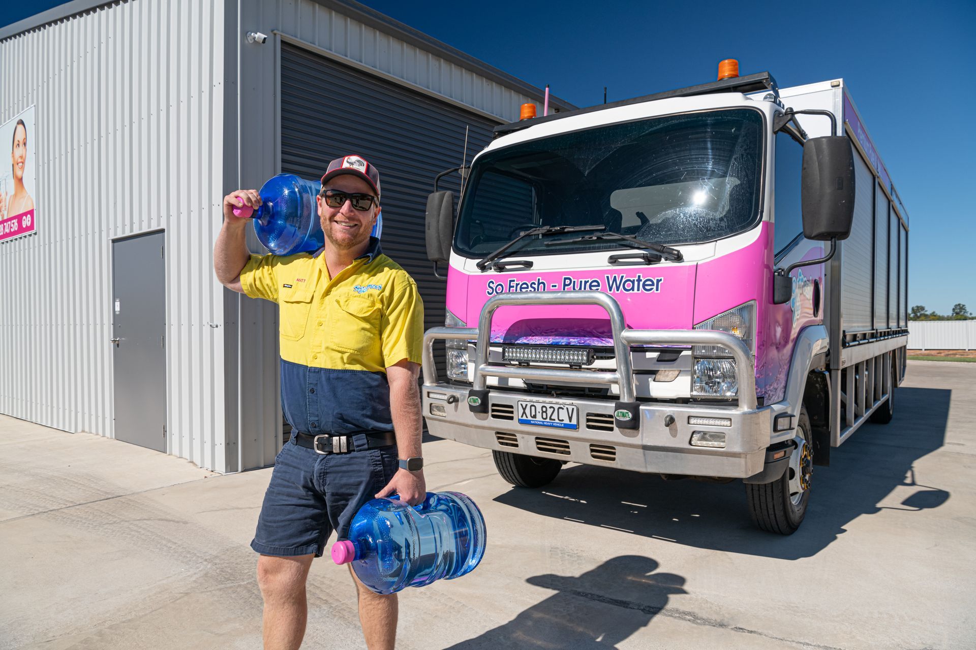 Person in yellow shirt holding water jugs beside a pink truck outside a warehouse